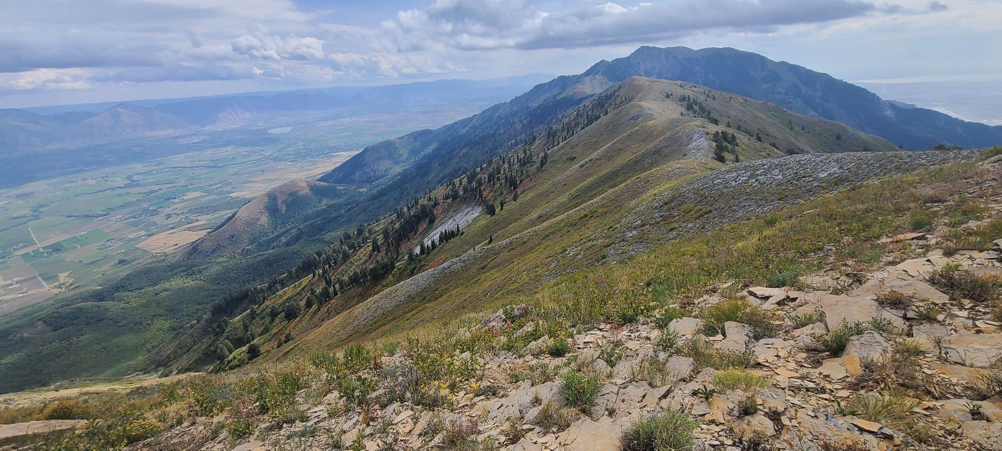 A long mountain ridge descends into a vast valley under a cloudy sky. - Mendon Peak Trail