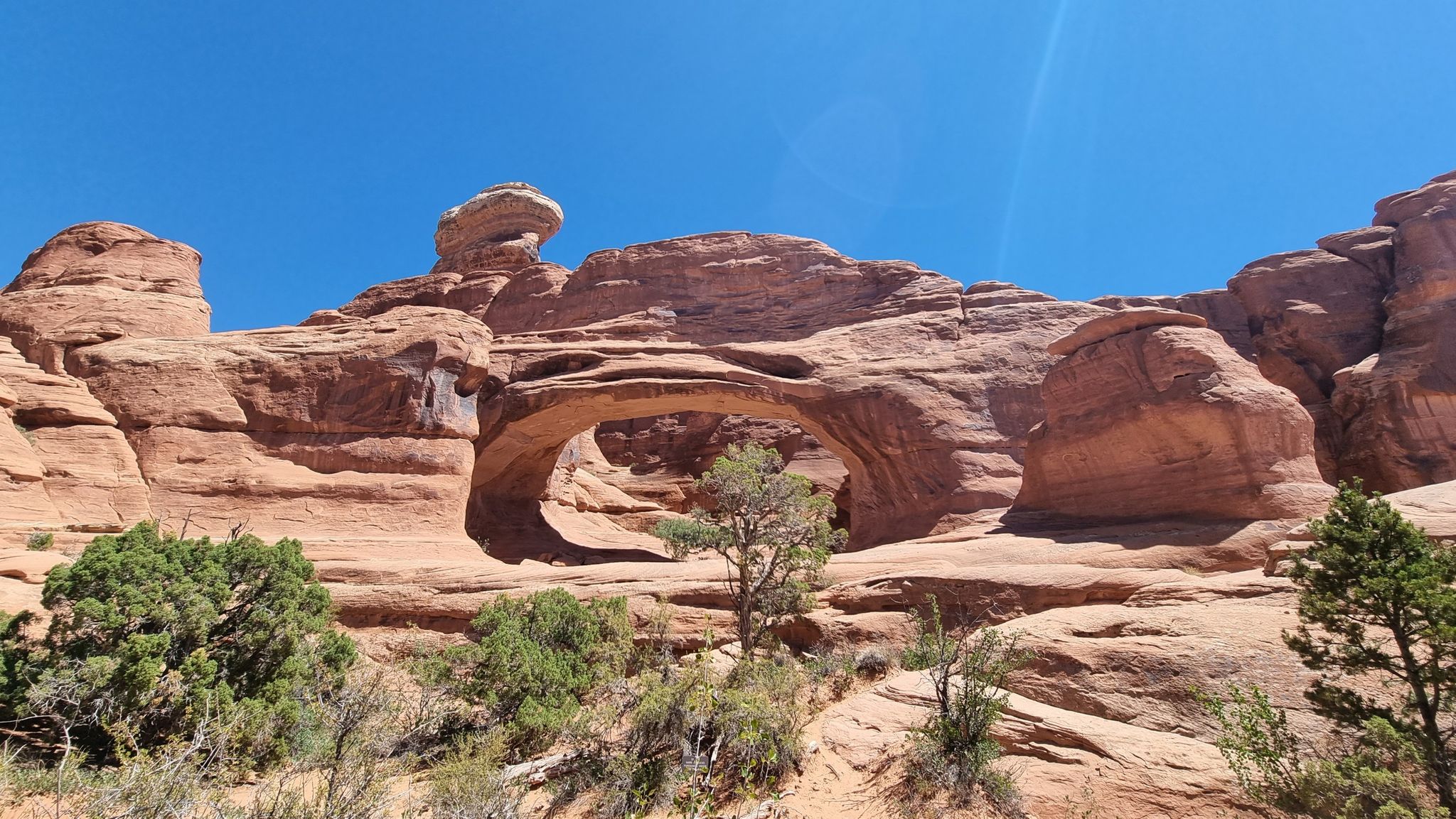 Bright desert scene with a large natural rock arch under a clear blue sky. - Lower Tower Arch Trail