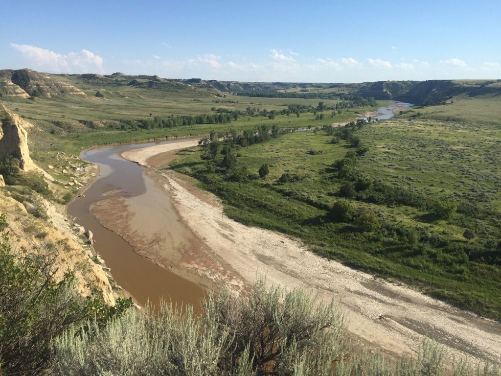 A wide, winding river flows through a green, sunny valley. - Wind Canyon Trail