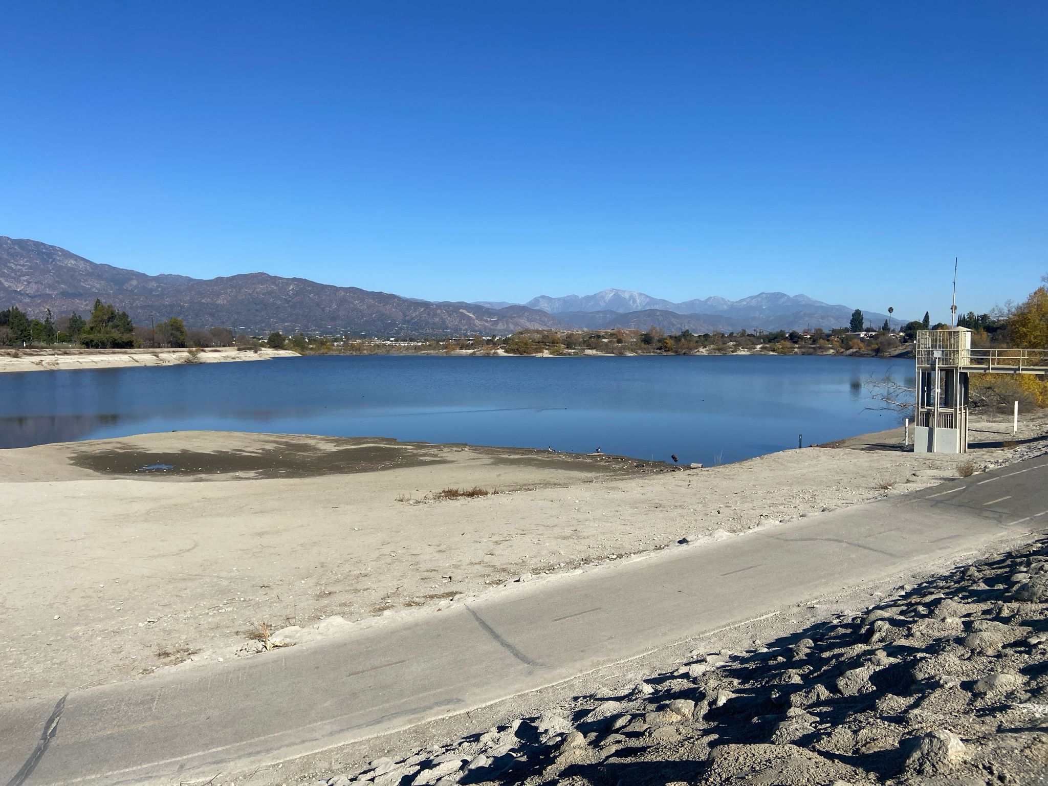 A wide lake with a sandy shore and distant mountains under a blue sky. - Bosque del Rio Hondo – Rio Hondo Greenway loop from Pio Pico Elementary School