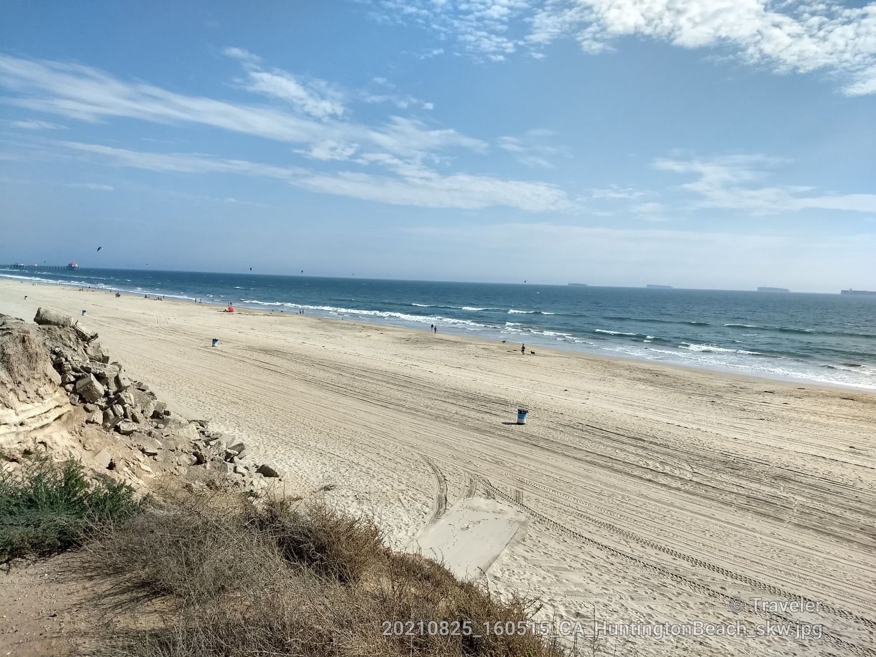 Wide sandy beach with ocean waves, blue sky, and distant people. Bright daylight. - Huntington Beach Bike Trail