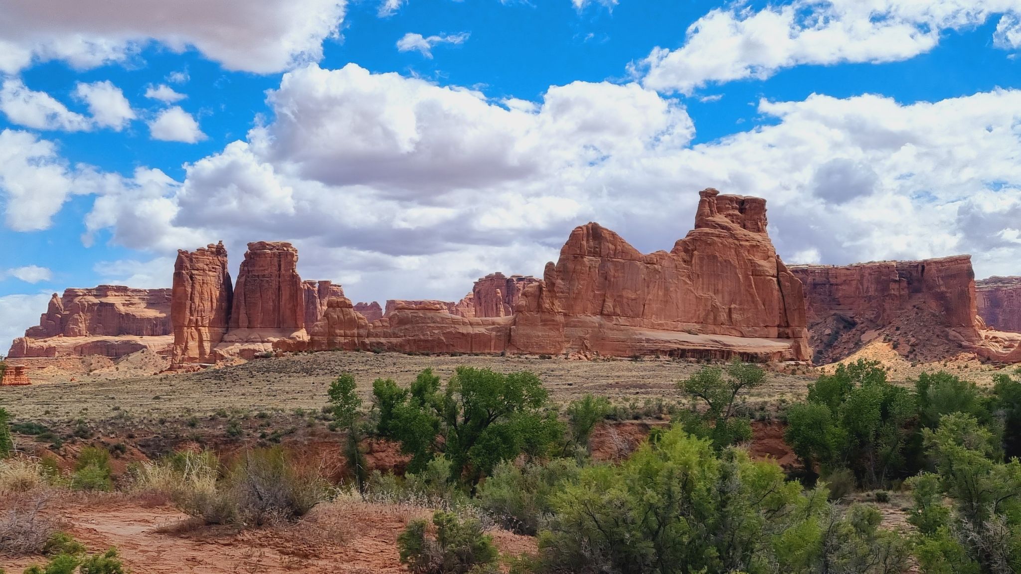 Vast desert landscape with towering red rock formations under a bright, cloudy sky. - The Tunnel