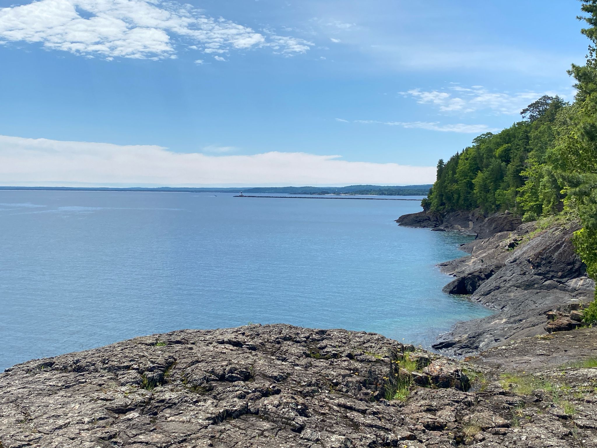 Expansive blue water meets a rocky, forested shoreline under a bright sky. - Presque Isle Park Loop