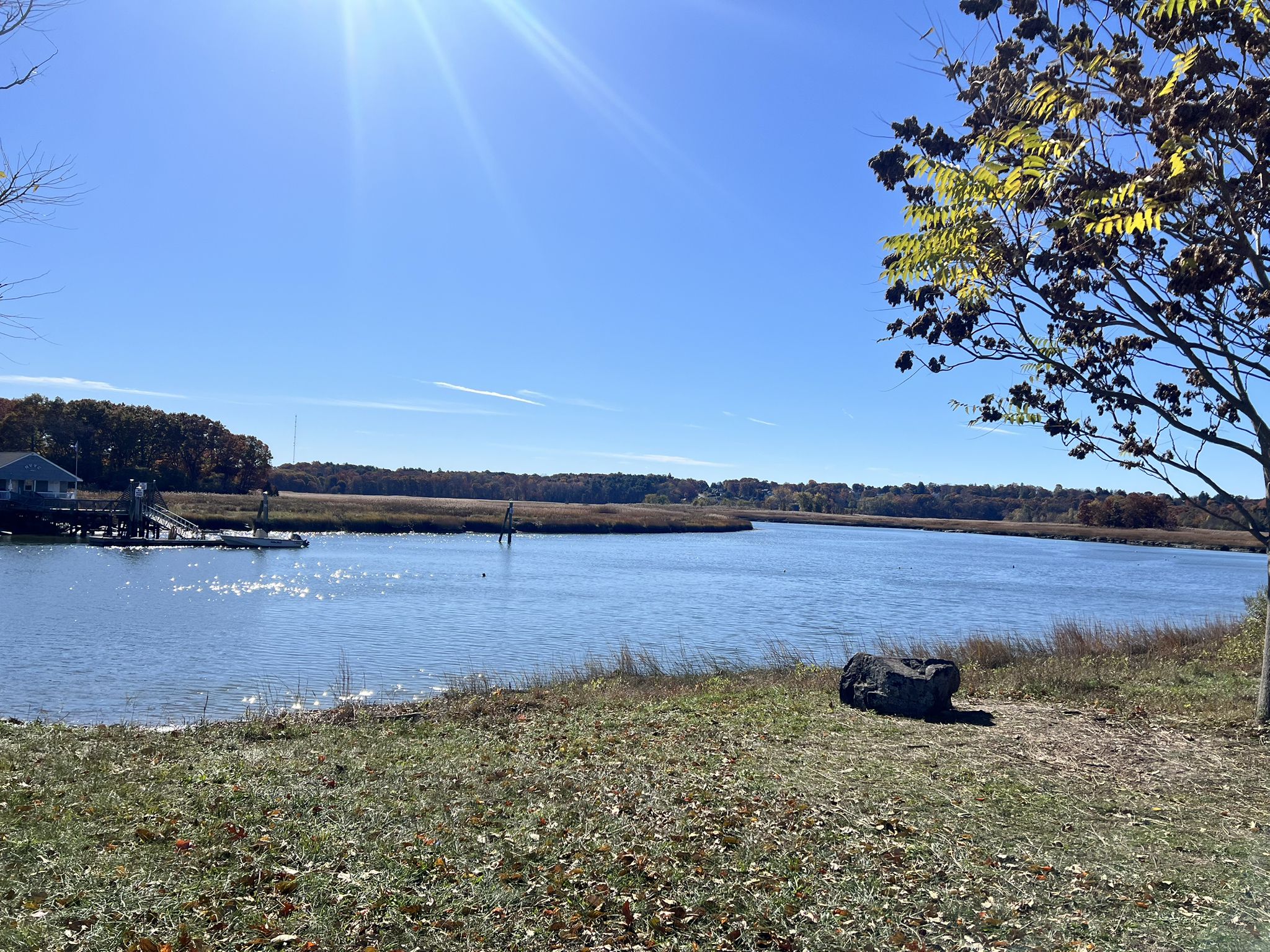 A wide river with a small dock and distant trees under a bright sunny sky. - Lower Neponset River Trail