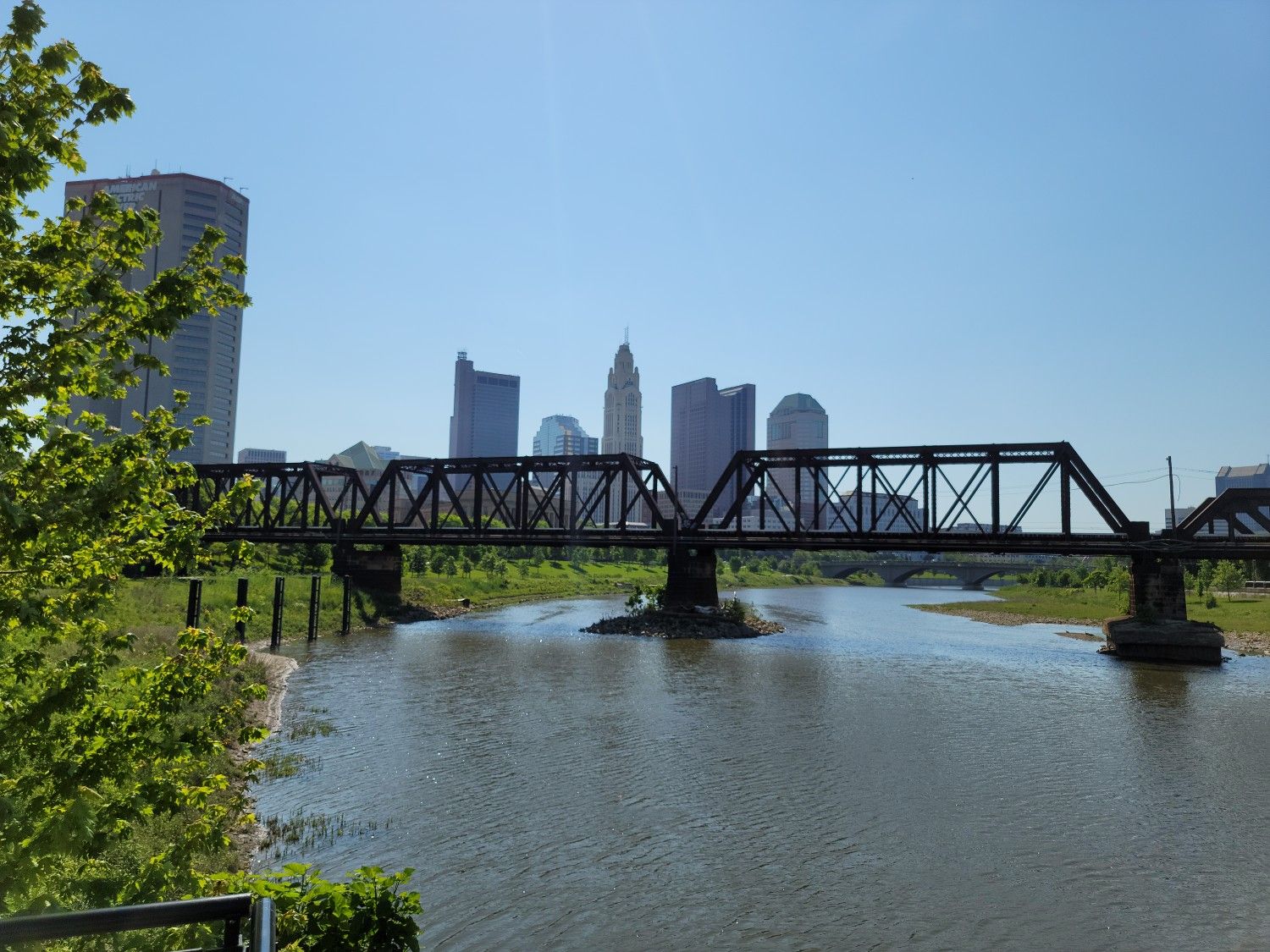 A city skyline rises behind a truss bridge over a calm river. - Franklin Park Conservatory – Franklin Park loop from Columbus