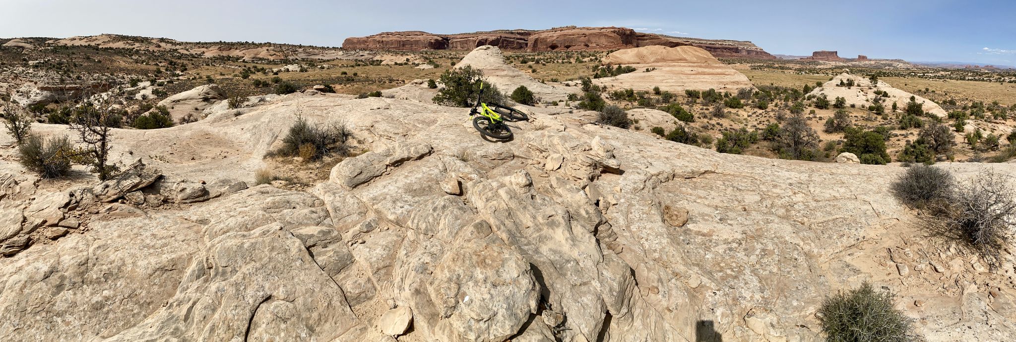 Mountain biker on a rocky desert outcrop with distant red rock formations. - Chisholm and Coney Island Trail Loop