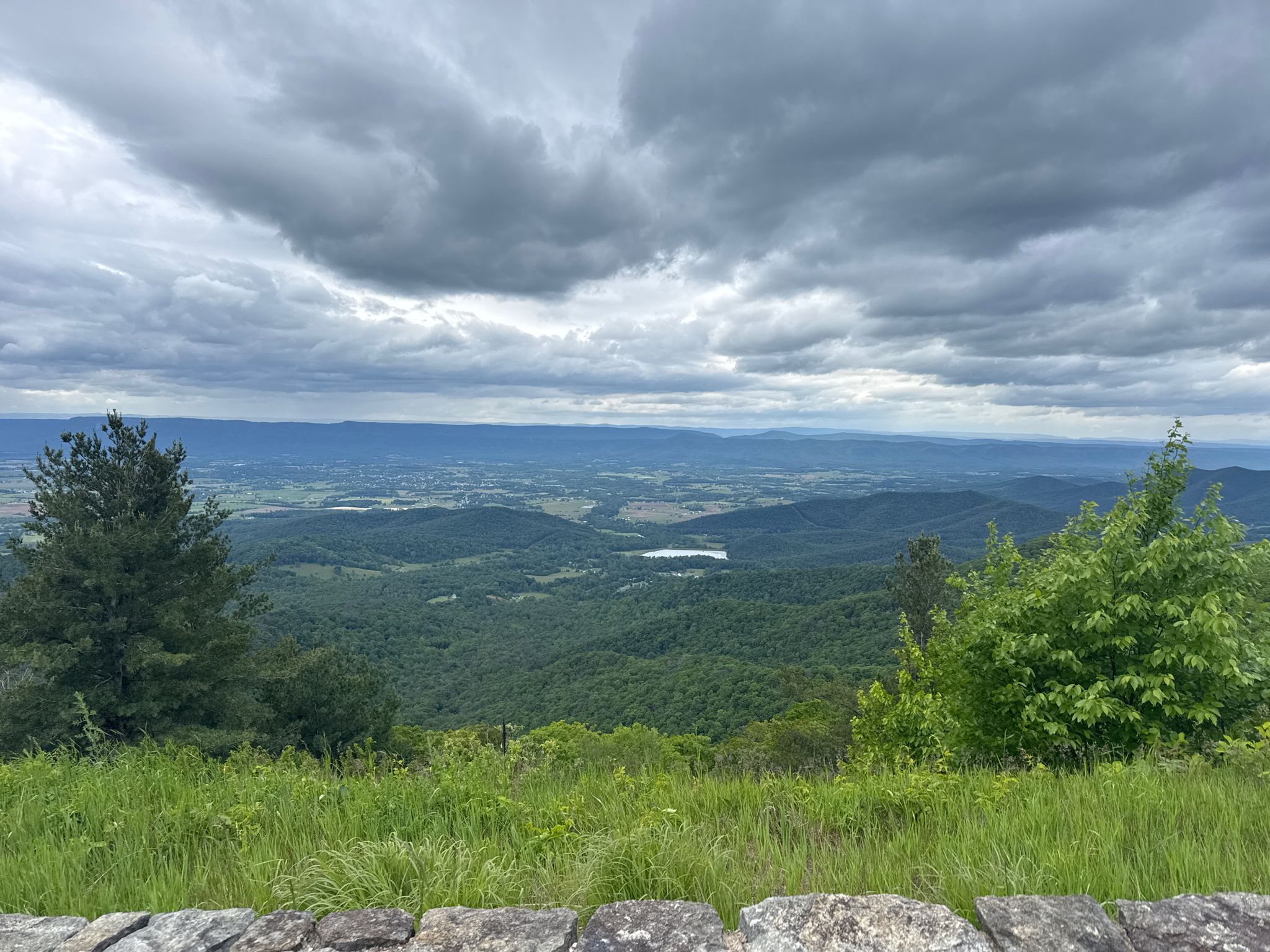Overcast mountain vista with green trees, distant valley, and small lake. - Highest Point on Skyline Drive – Crescent Rock Overlook loop from Sperryville