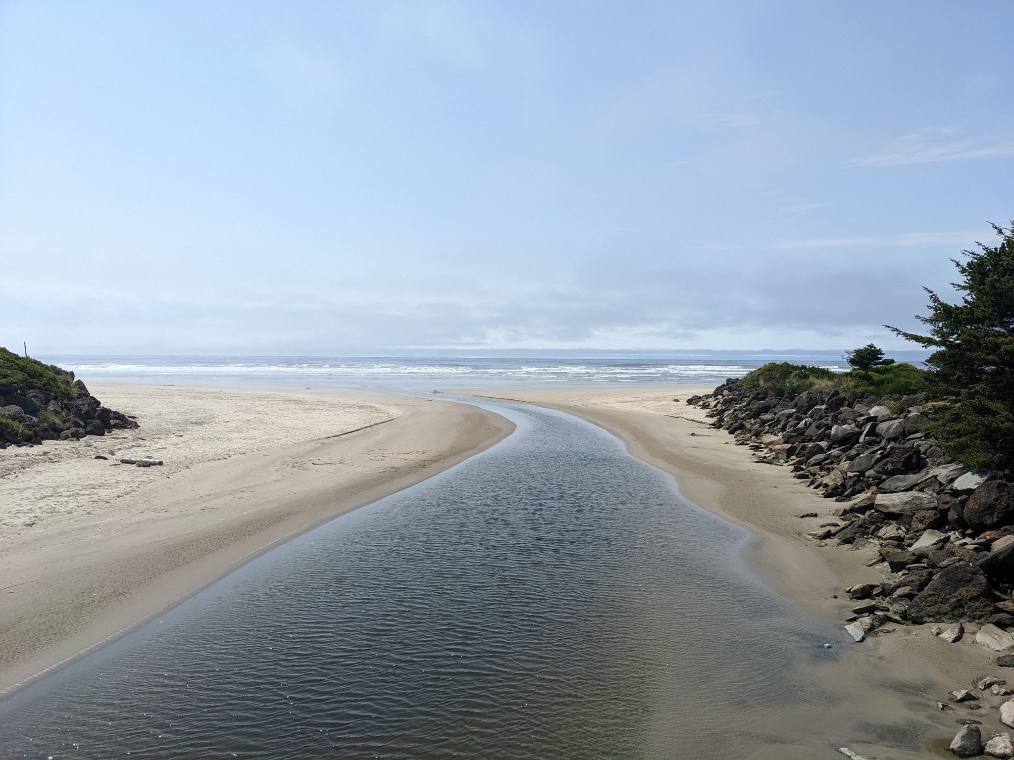 A calm river flows through sandy banks towards the ocean under a bright sky. - Gravel loop from Beachside State Recreation Site