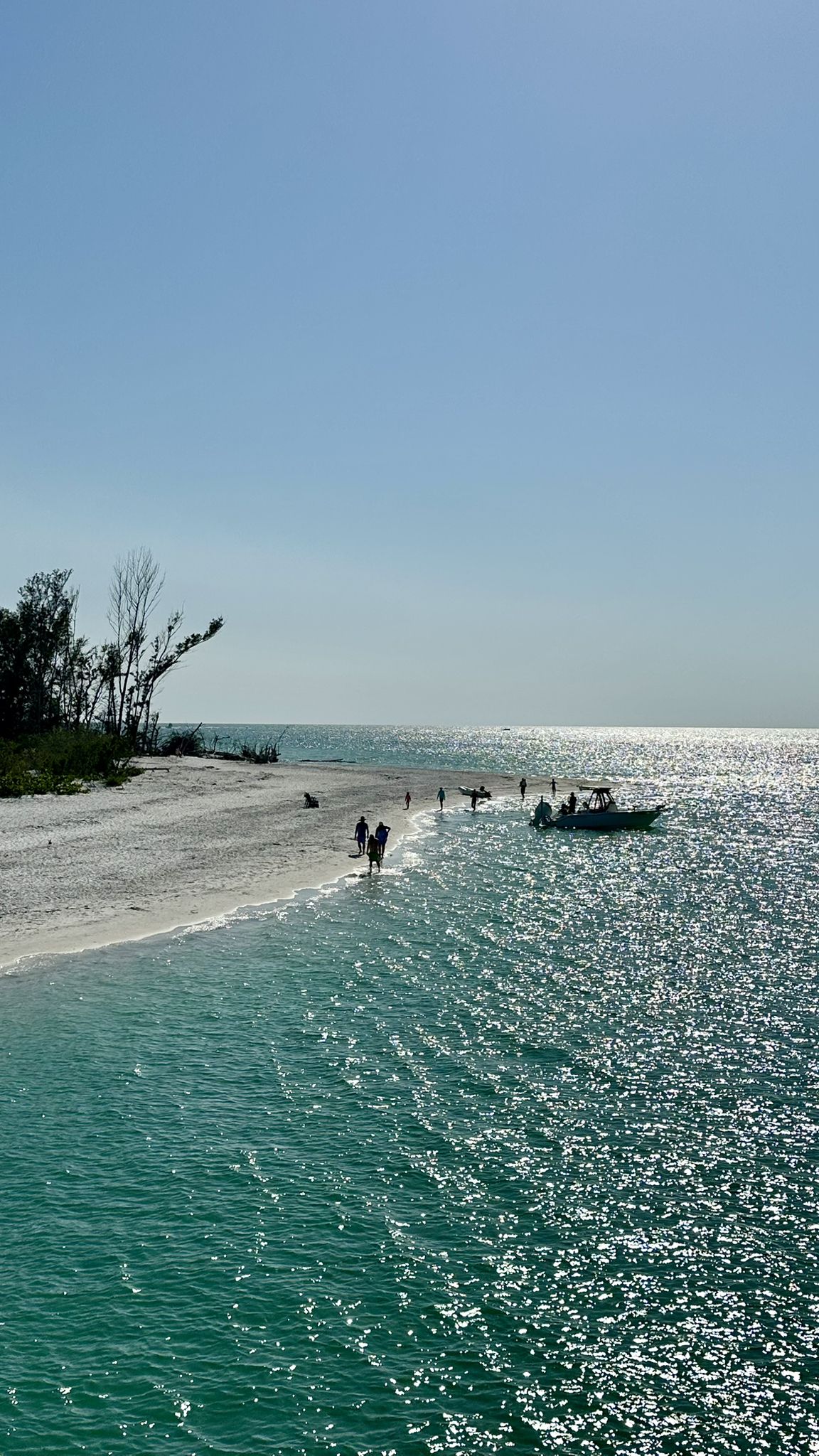 People wading in sparkling turquoise water next to a sandy shoreline and boat. - Bayfront Park – Longboat Key loop from Mattison's
