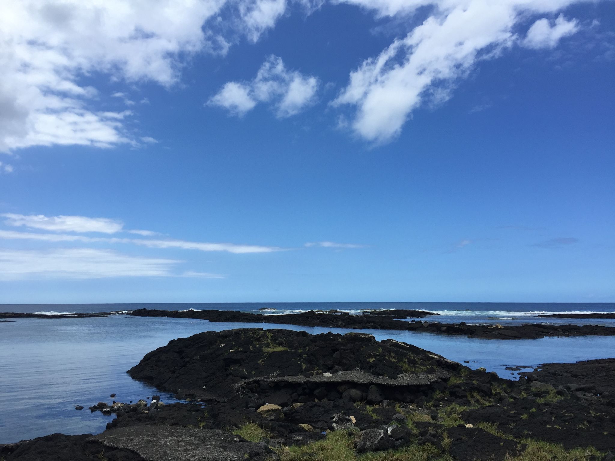 Bright coastal scene with dark volcanic rock formations in calm ocean pools. - Onekahakaha Beach Park via Kalanianaole Street loop