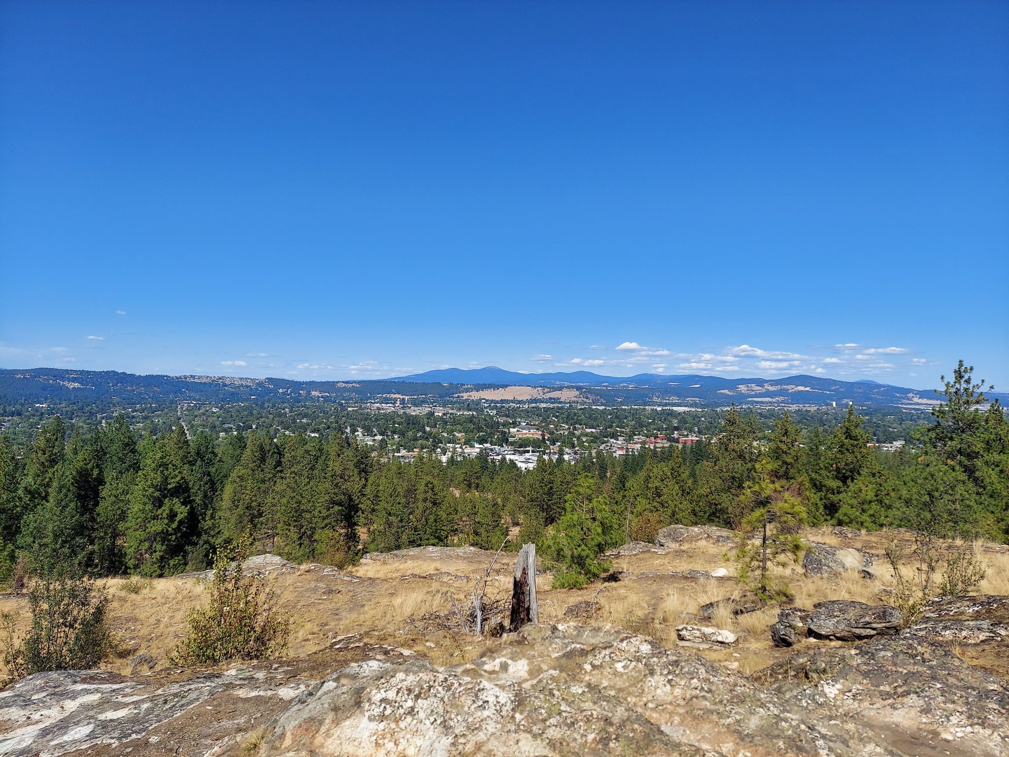 Sunny panoramic view from rocky hilltop overlooking a town and mountains. - Pond Loop Trail loop from Dishman