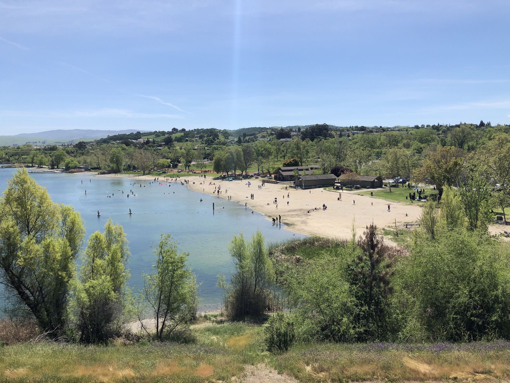 Sunny day at a busy lake beach with many people swimming and relaxing. - Iron Horse Regional Trail