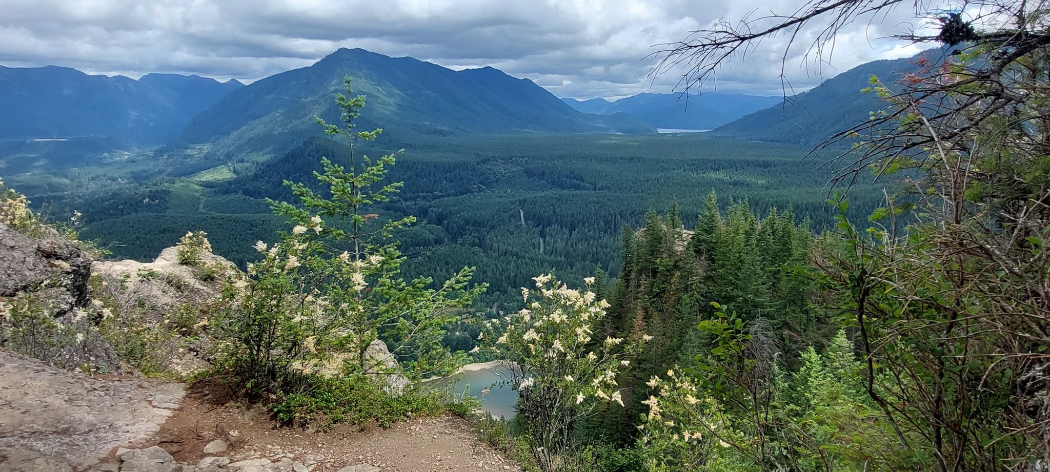Panoramic view of a forested mountain valley with a lake under cloudy skies. - Rattlesnake Ledge Trail