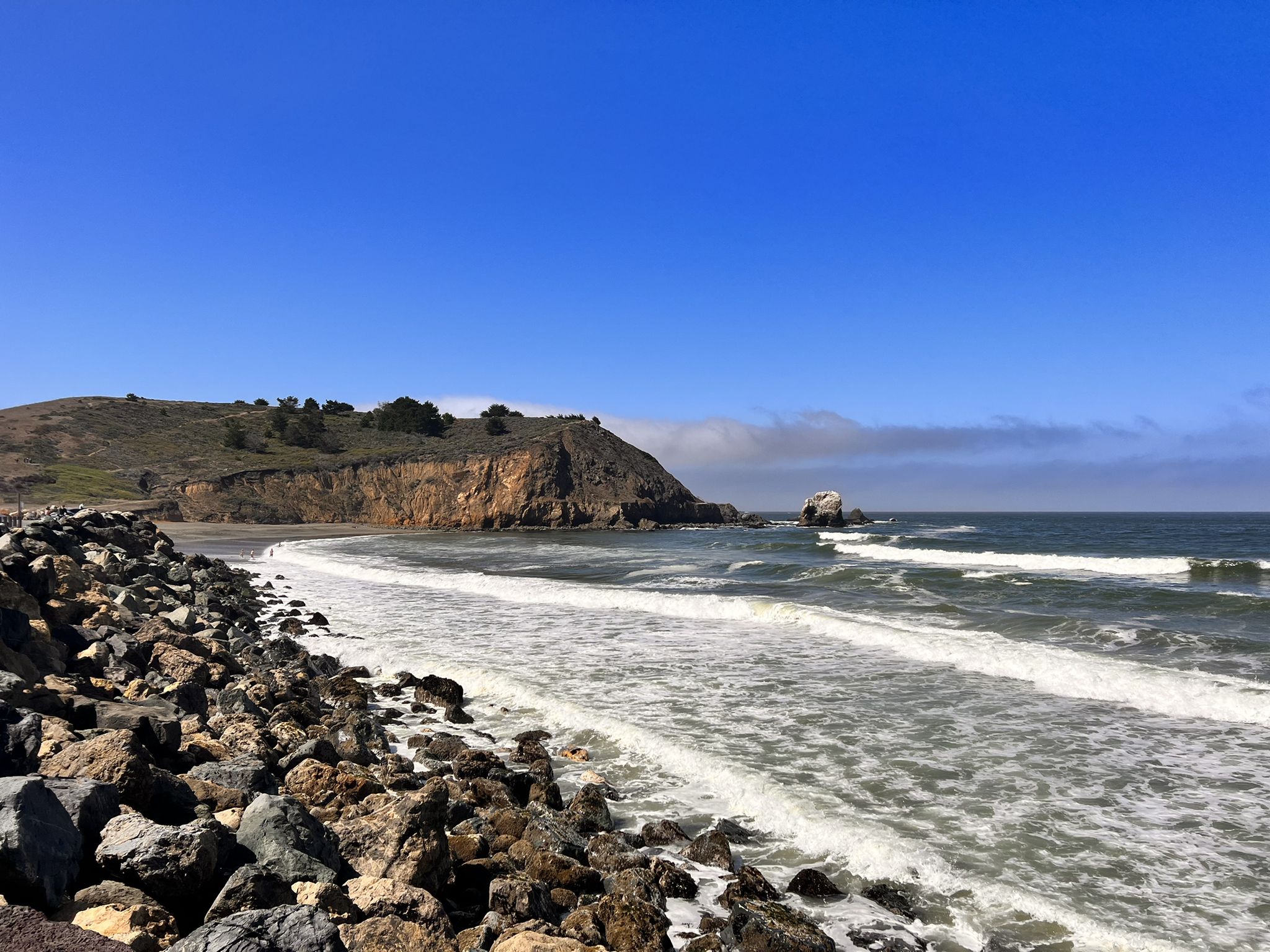 Waves break on a rocky beach with cliffs and a clear blue sky. - Mori Point Headlands – Rockaway Beach loop from Serramonte Center