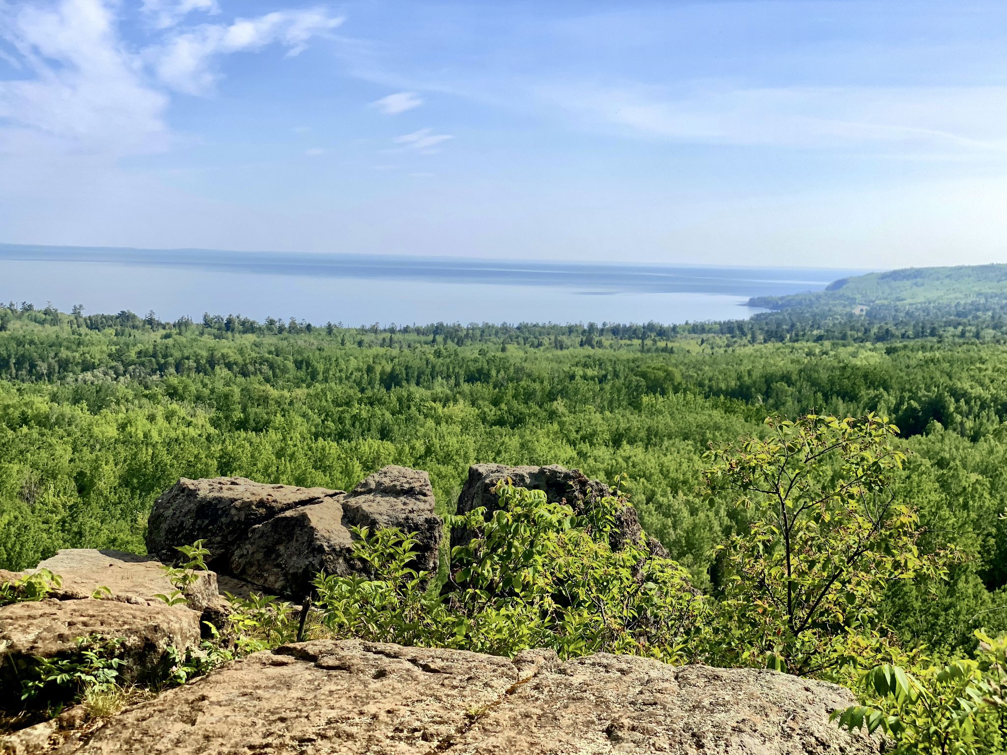 Overlook of vast green forest, large body of water, and bright sky. - Superior Hiking Trail