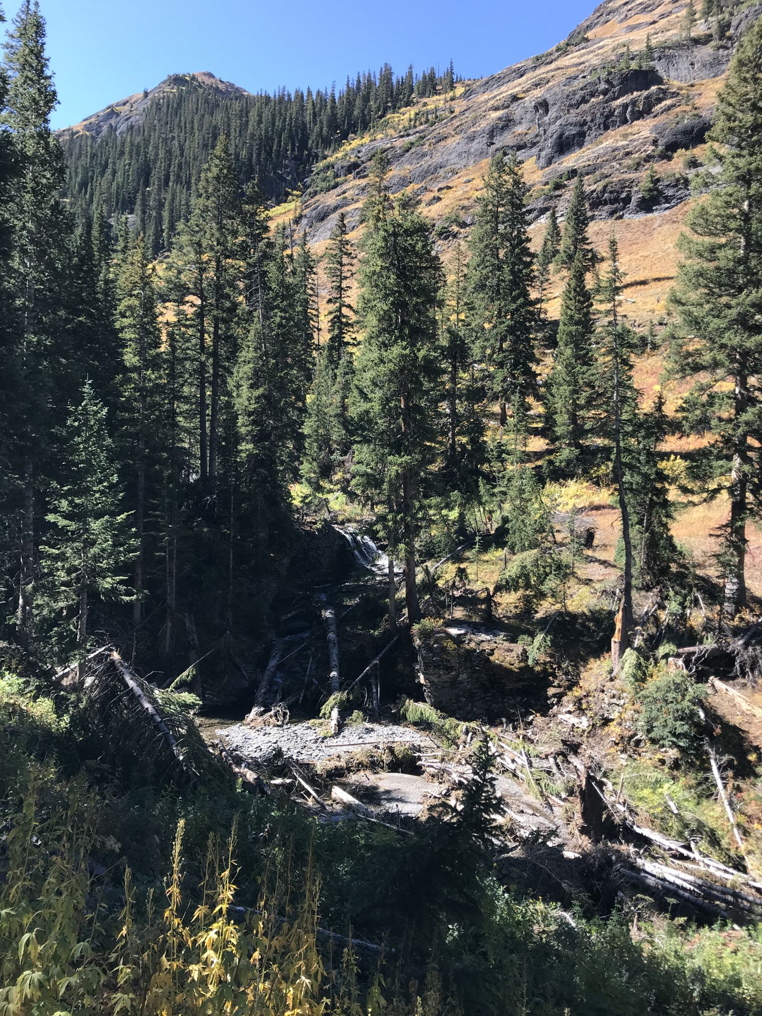 Waterfall cascading down a rocky, forested mountainside in bright sunlight. - Blue Lake via Bridal Veil Trail