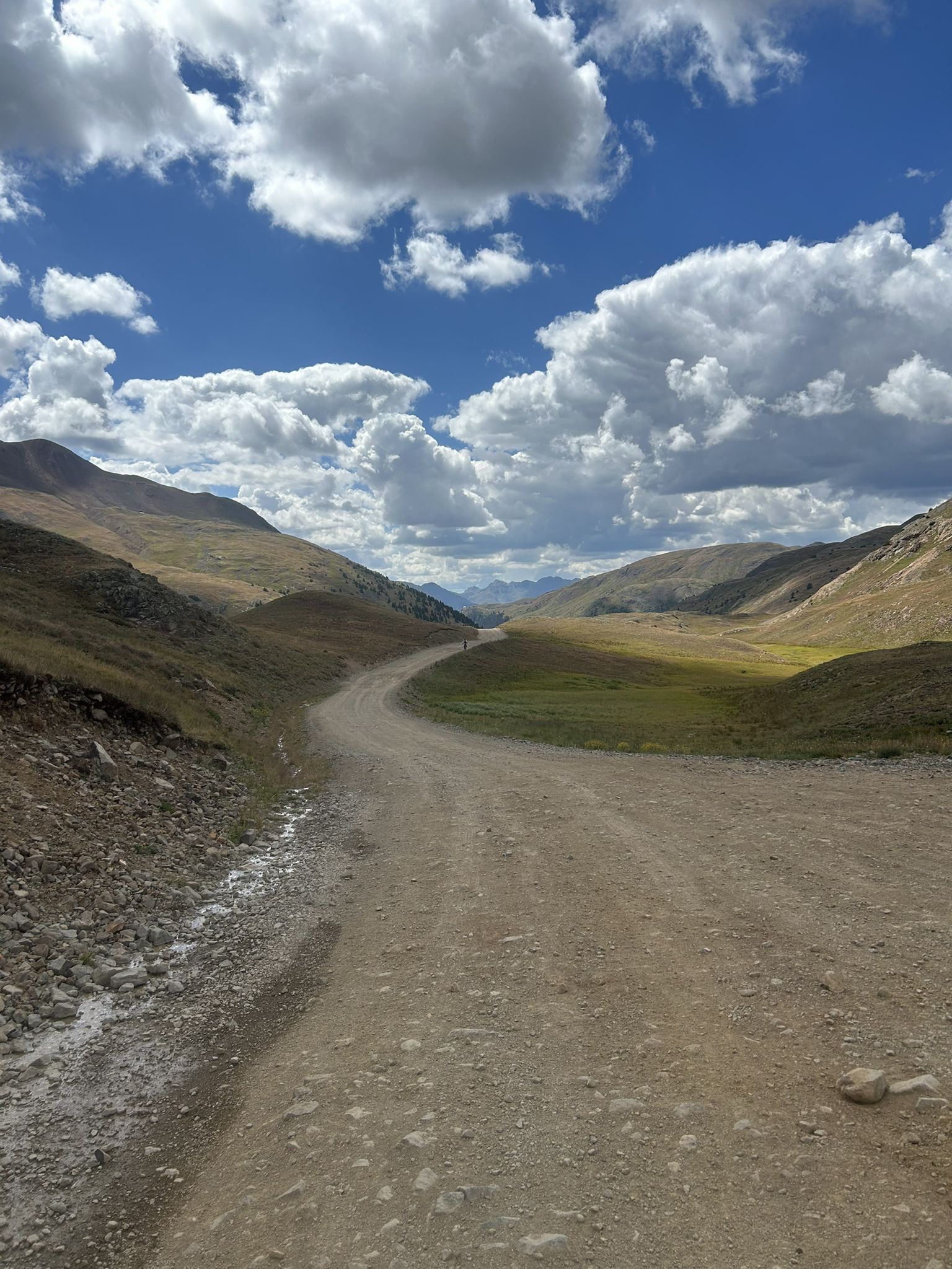 A dirt road winds through a sunny mountain valley under a cloudy sky. - Mineral Creek OHV Trail