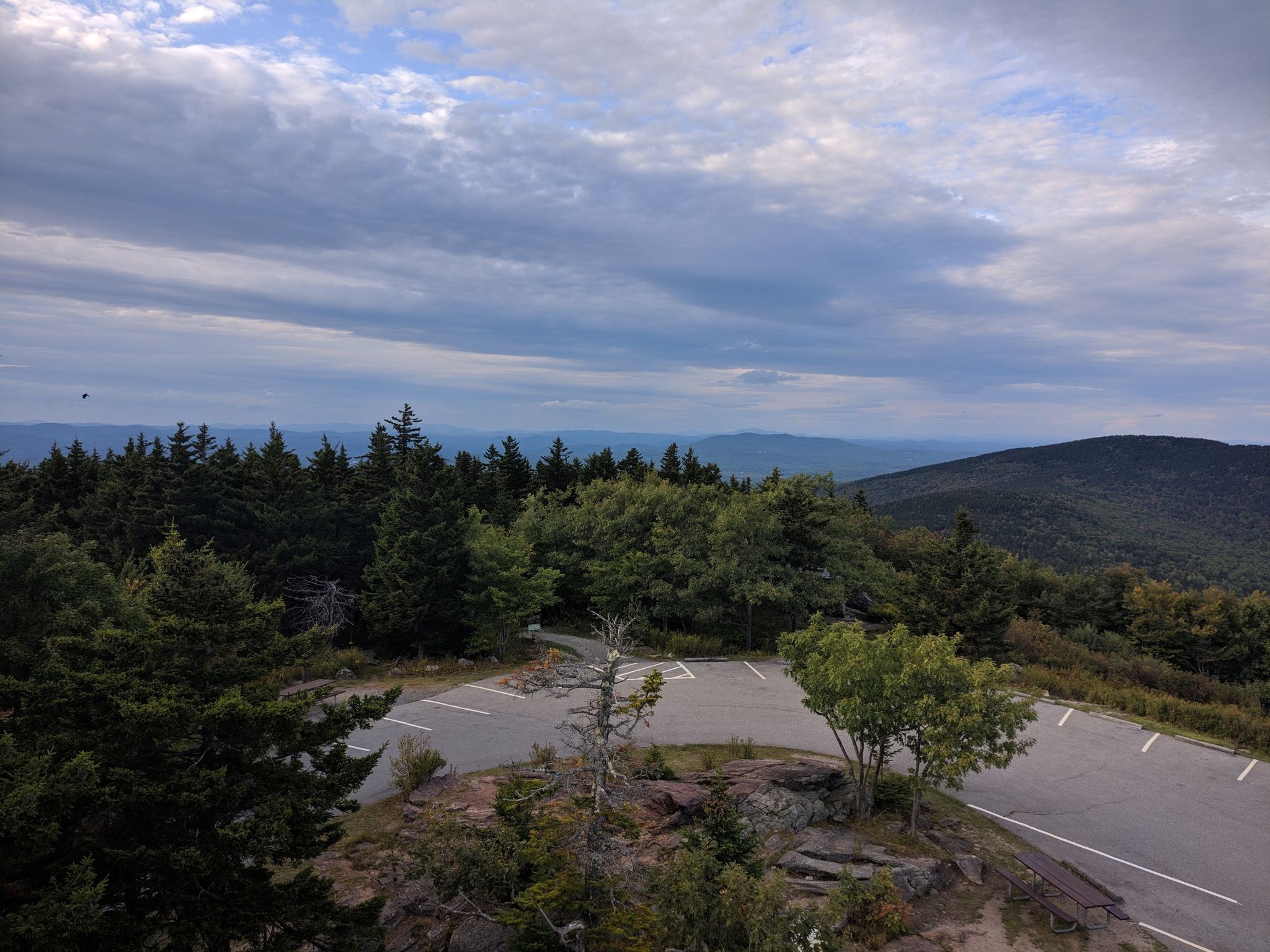 Overcast sky above a mountain vista with a paved parking area and dense forest. - Milford to Pack Monadnock Mountain loop