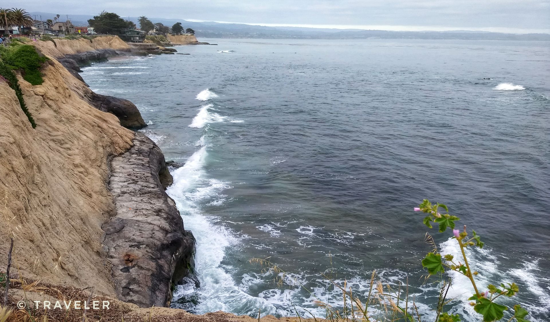Waves crashing against a rugged, rocky cliff under a cloudy sky. - East Cliff Drive County Parkway