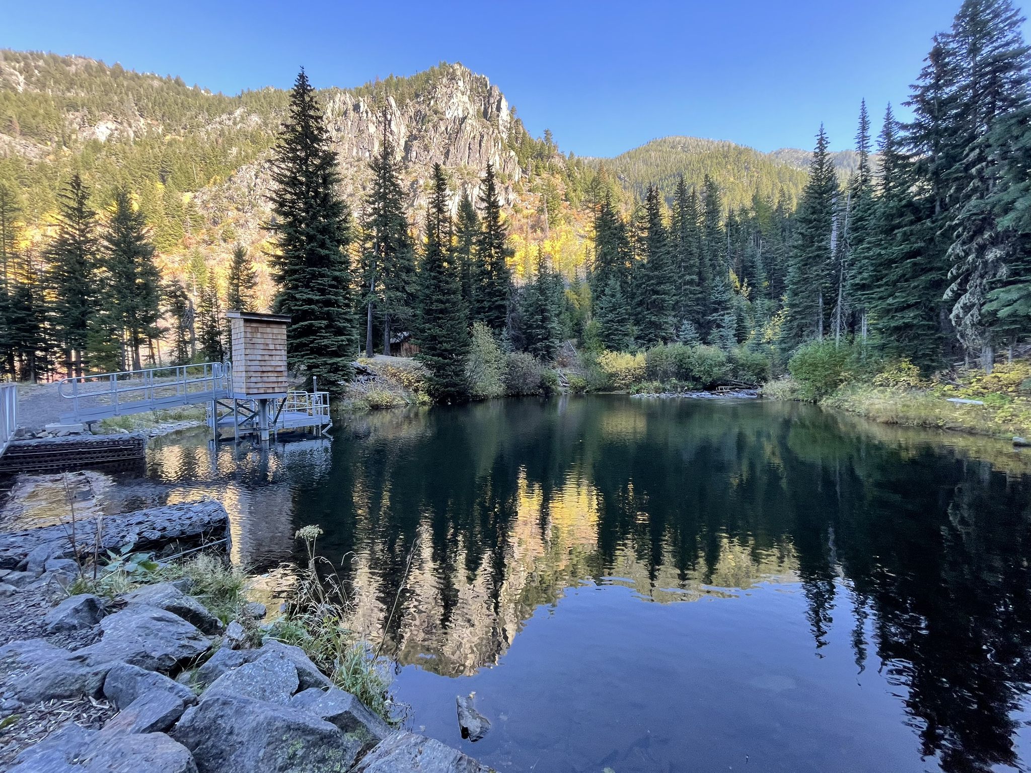 Calm lake reflecting mountains and trees, with a small building on a dock. - East Fork Wallowa Trail