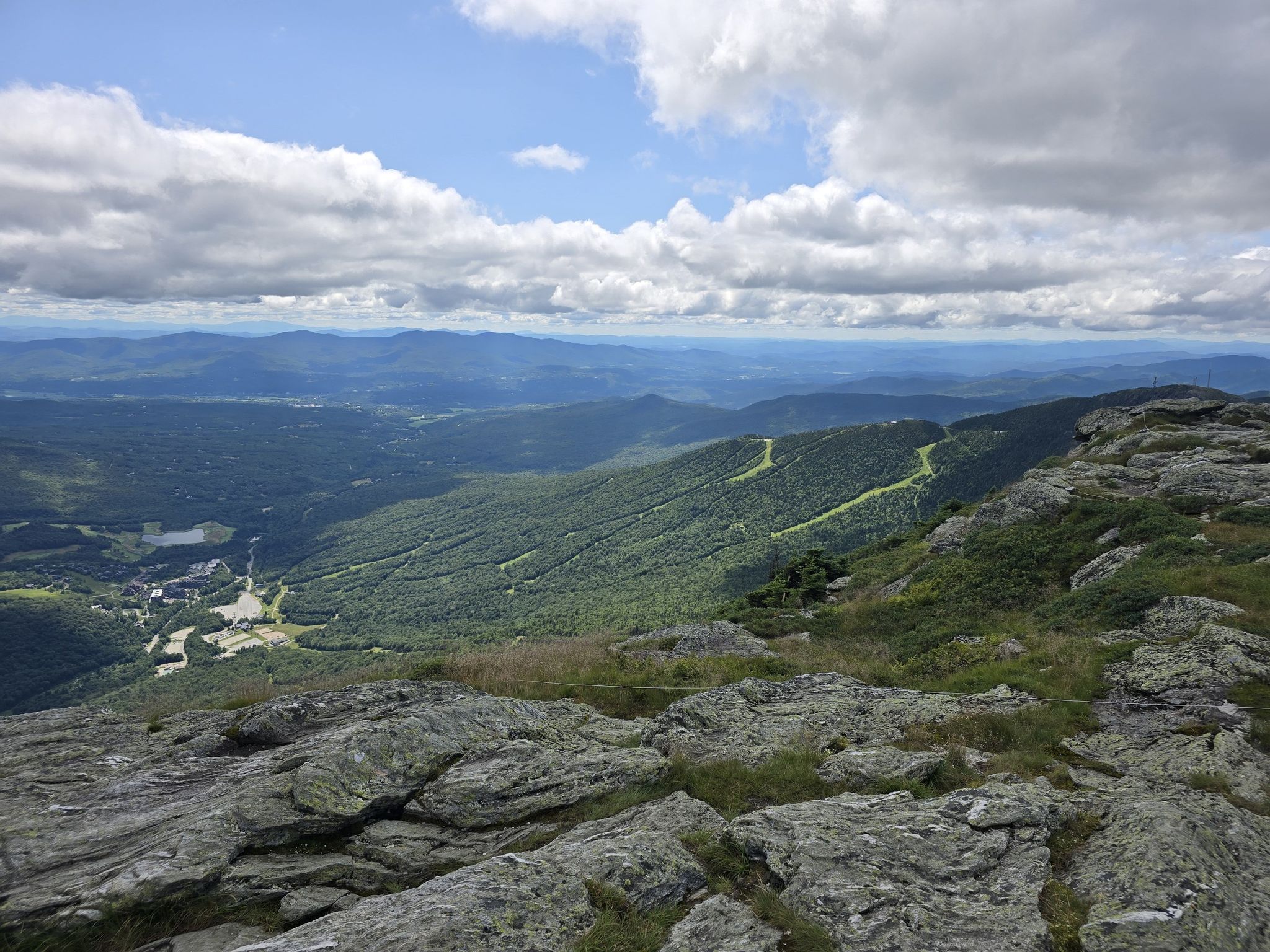 Expansive mountain view with rocky foreground, green forests, and ski trails. - Mansfield's Adam's Apple – Mount Mansfield Summit loop from Mount Mansfield