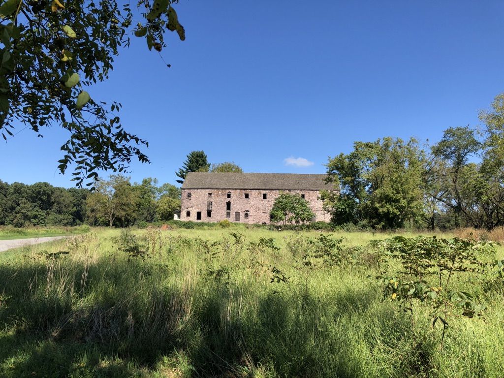 Large stone building in a sunny green field, surrounded by trees. - Commissary and Fatlands Trail Loop