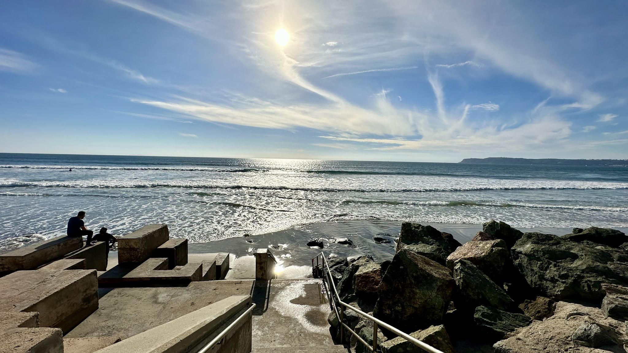 Concrete steps to the ocean, people sitting, and sun reflecting on the water. - Coronado Shores Beach – Hotel del Coronado loop from Coronado