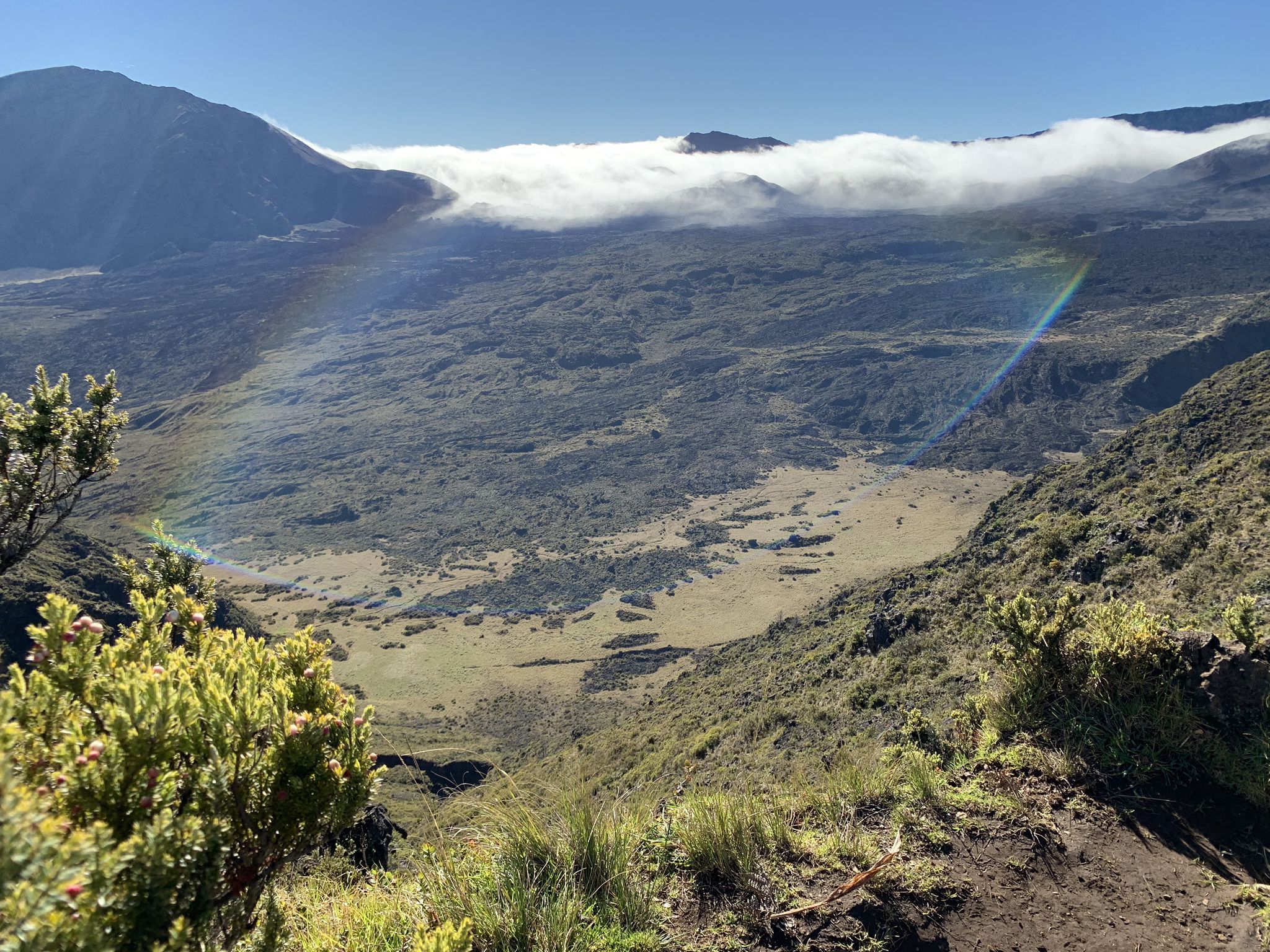An expansive valley with a faint rainbow under a bright sky. - Halemauʻu Trail