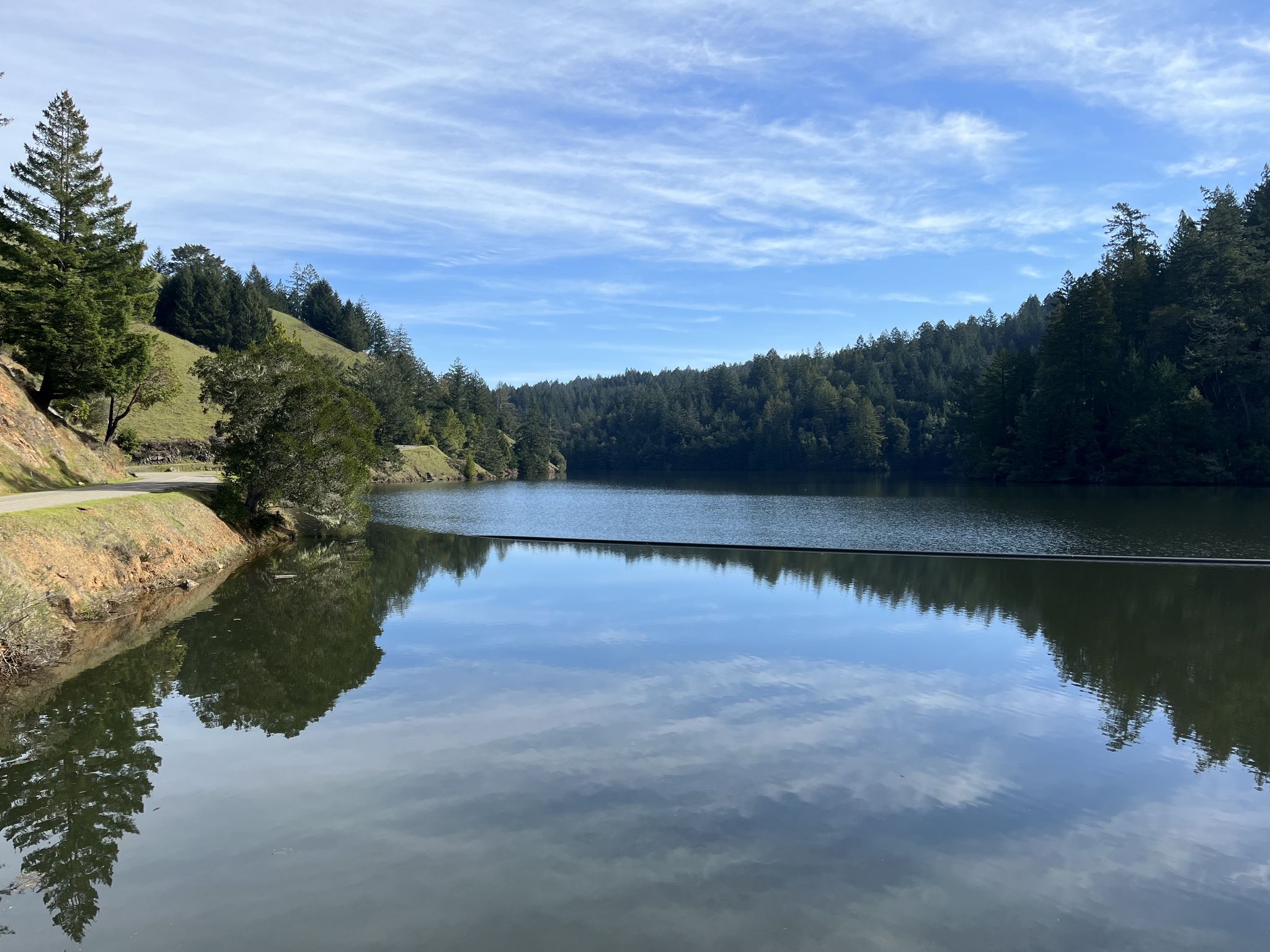 Calm lake reflecting sky, surrounded by green hills and dense forest. - Alpine Lake – Alpine Dam loop from Fairfax