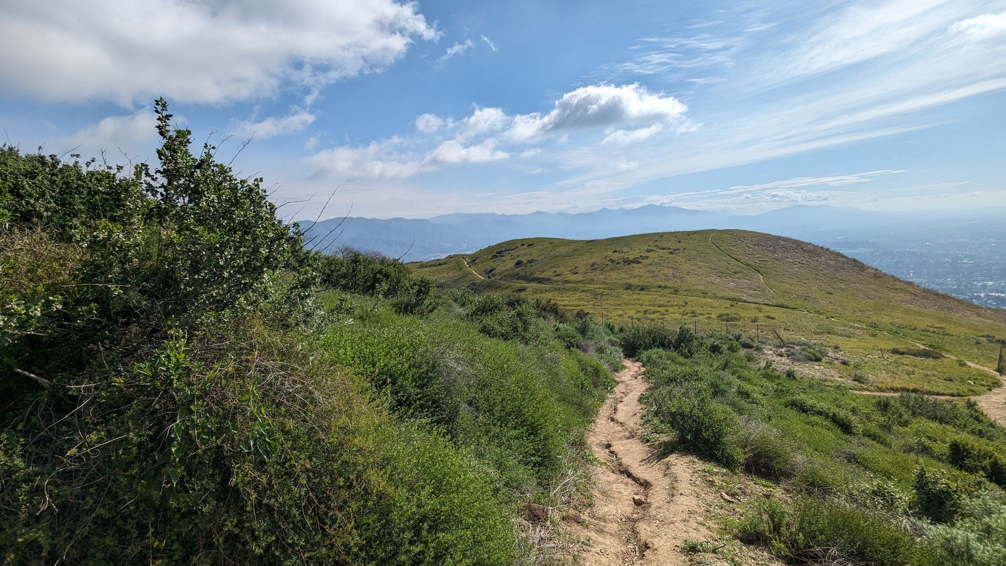 A dirt path on a green hillside with distant mountains under a cloudy sky. - O'Melveny Park to Mission Point Loop