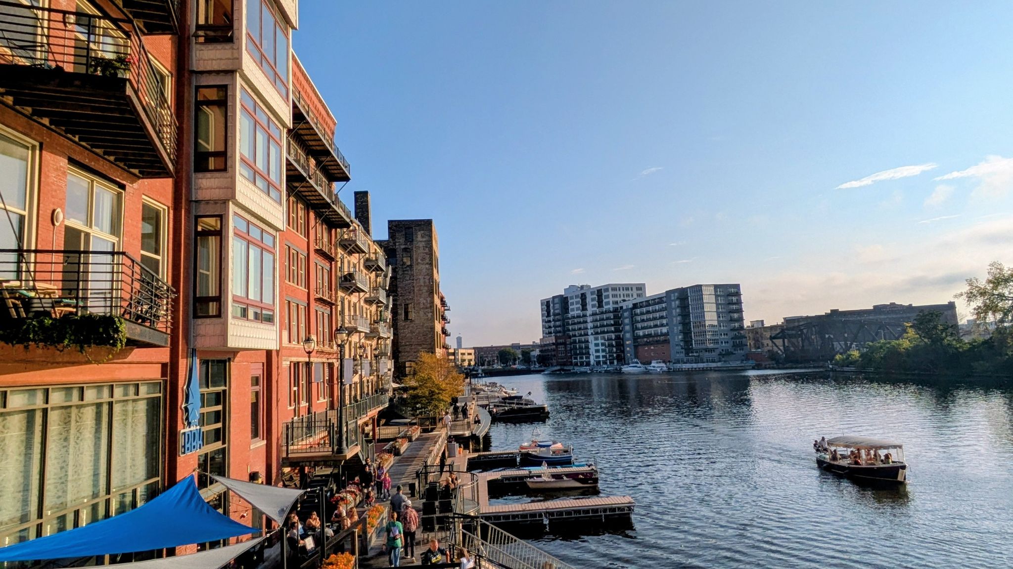 Sunny view of a river with buildings, docks, and a small boat. - Pebble Beach – Milwaukee Pierhead Lighthouse loop from Milwaukee