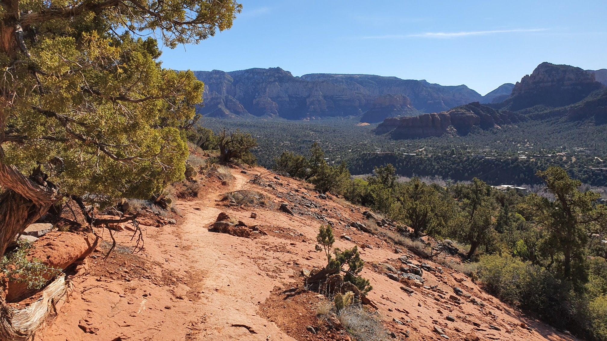 Sunny red dirt trail overlooking a vast green valley and distant mountains. - Brewer Trail