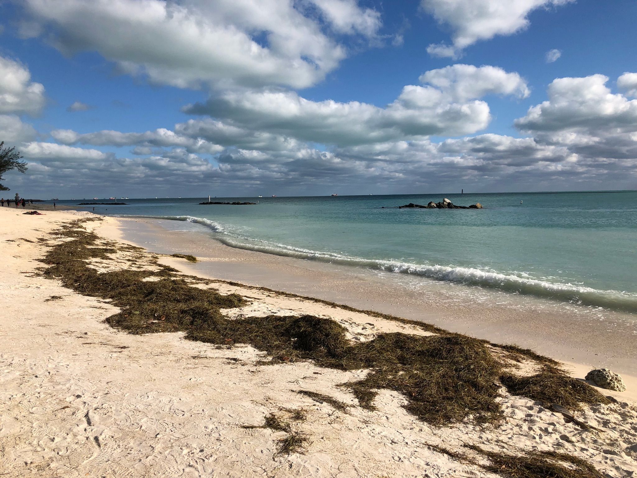 Sandy beach with seaweed, turquoise ocean, and cloudy blue sky. - Southernmost Point Buoy – Southernmost Point loop from Key West