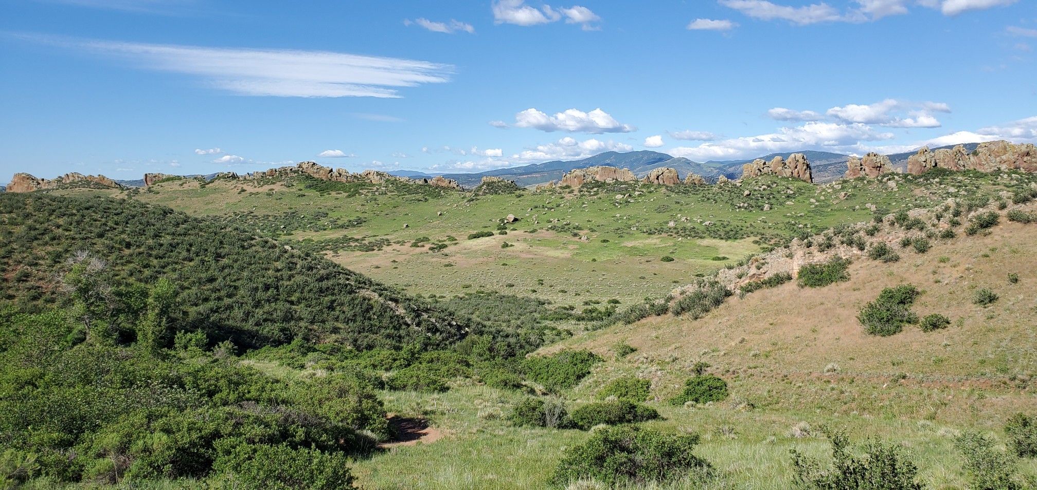 Sunny panoramic view of green rolling hills and distant rock formations. - Devils Backbone Open Space – Blue Sky Trail viewpoint loop from Loveland Transit Center