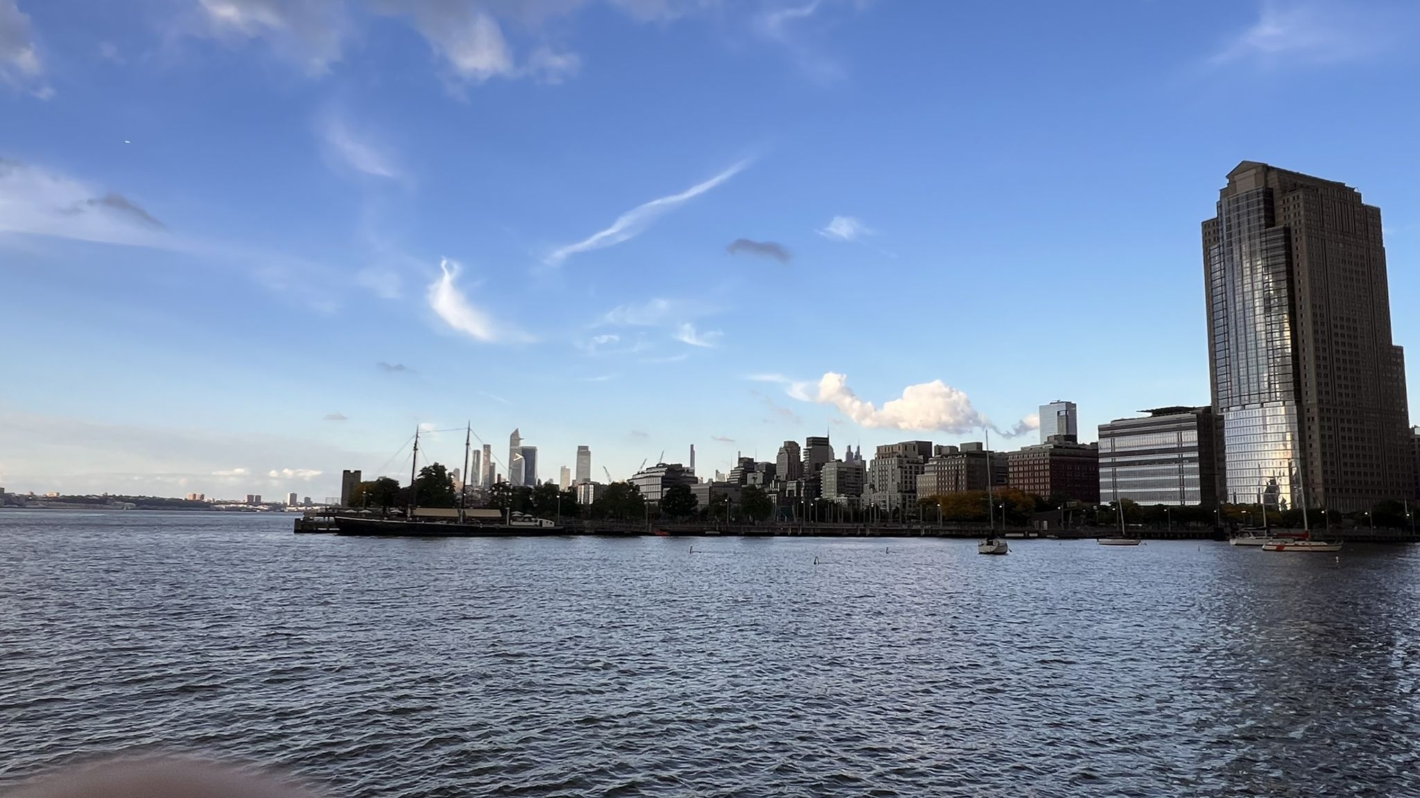 City skyline across water under a partly cloudy blue sky. - Battery Park and Battery Park City Greenway Loop