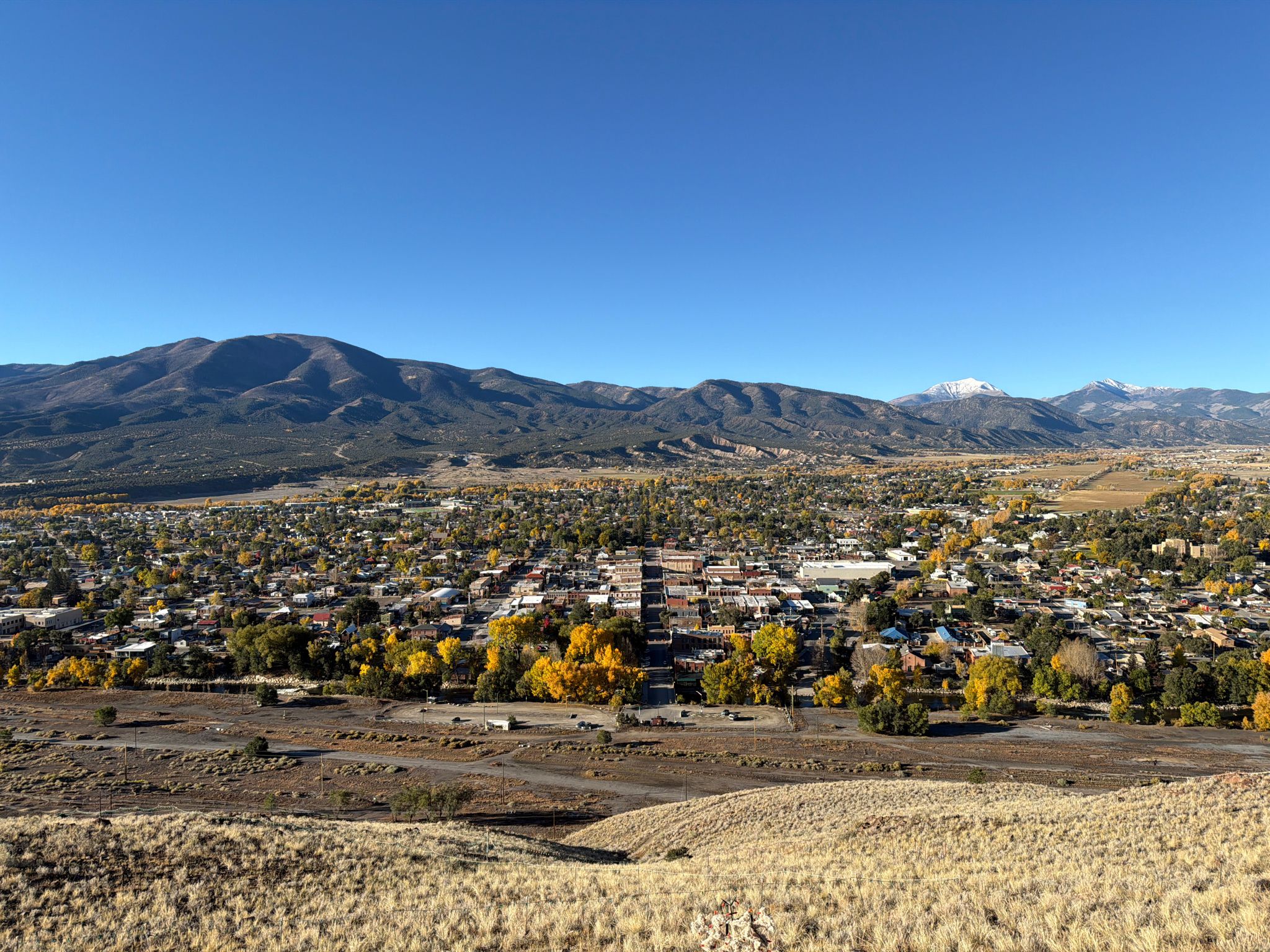 Elevated view of a town with vibrant autumn trees, backed by large mountains. - Pole Line Trail