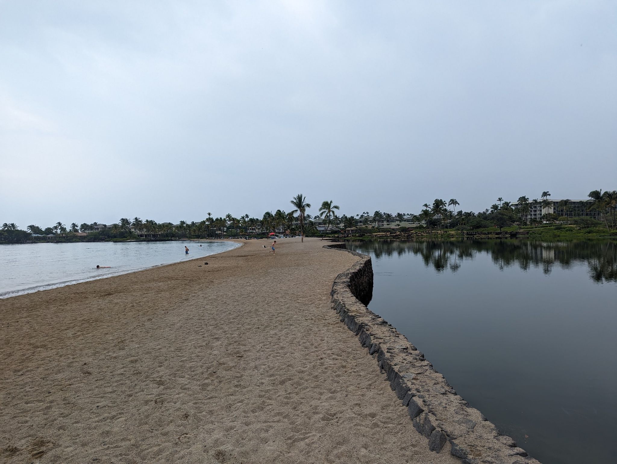 Sandy beach path separating ocean from calm water under an overcast sky. - Anaehoomalu Beach – Kuʻualiʻi Fishpond loop from Kamehameha V (1830 - 1872)