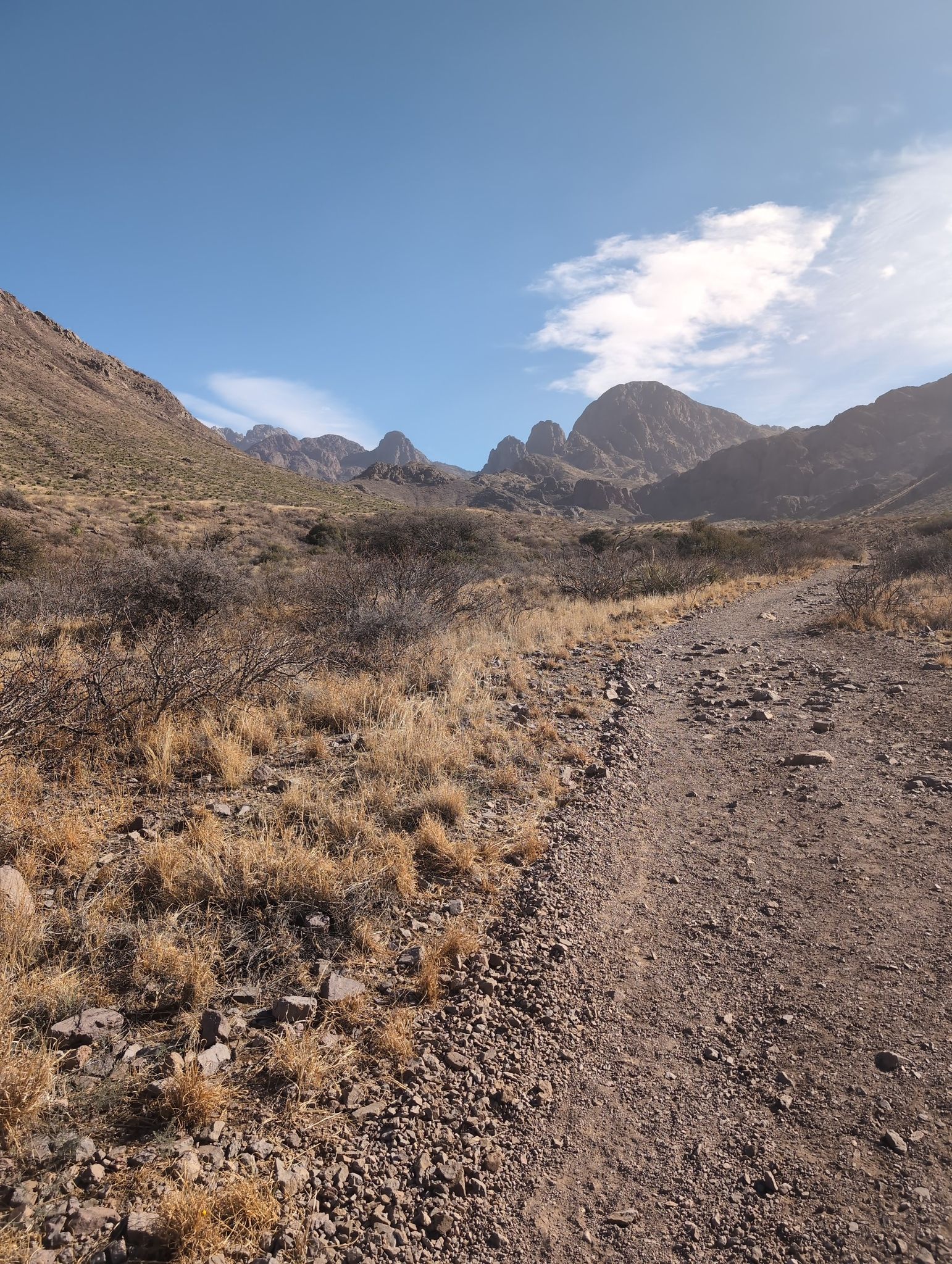 A rocky dirt path leads through an arid mountain landscape under a bright sky. - Bar Canyon