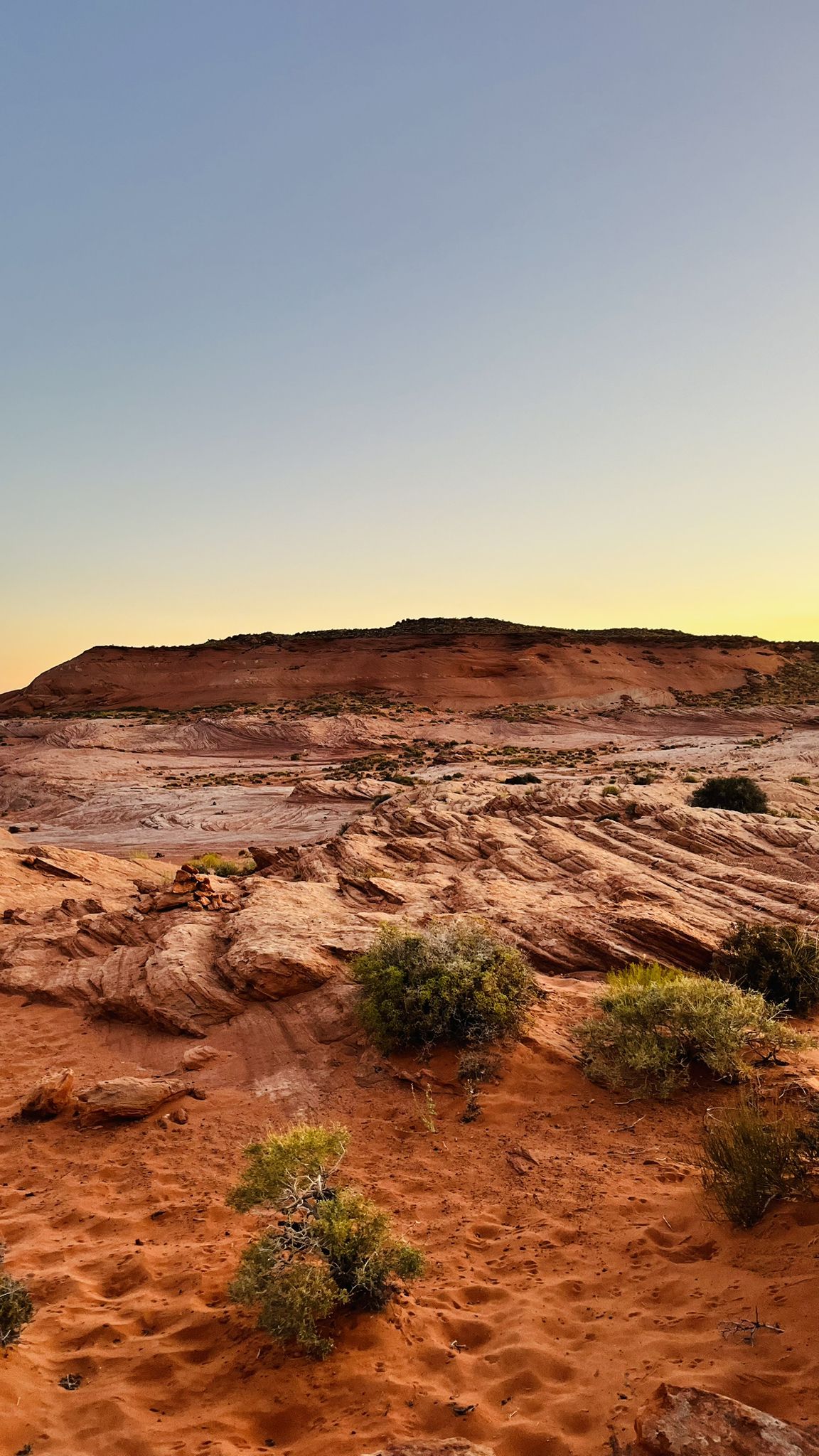 Arid desert landscape with red rock formations and sparse green shrubs under a clear sky. - Coyote Gulch - Jacob Hamblin Arch Trail