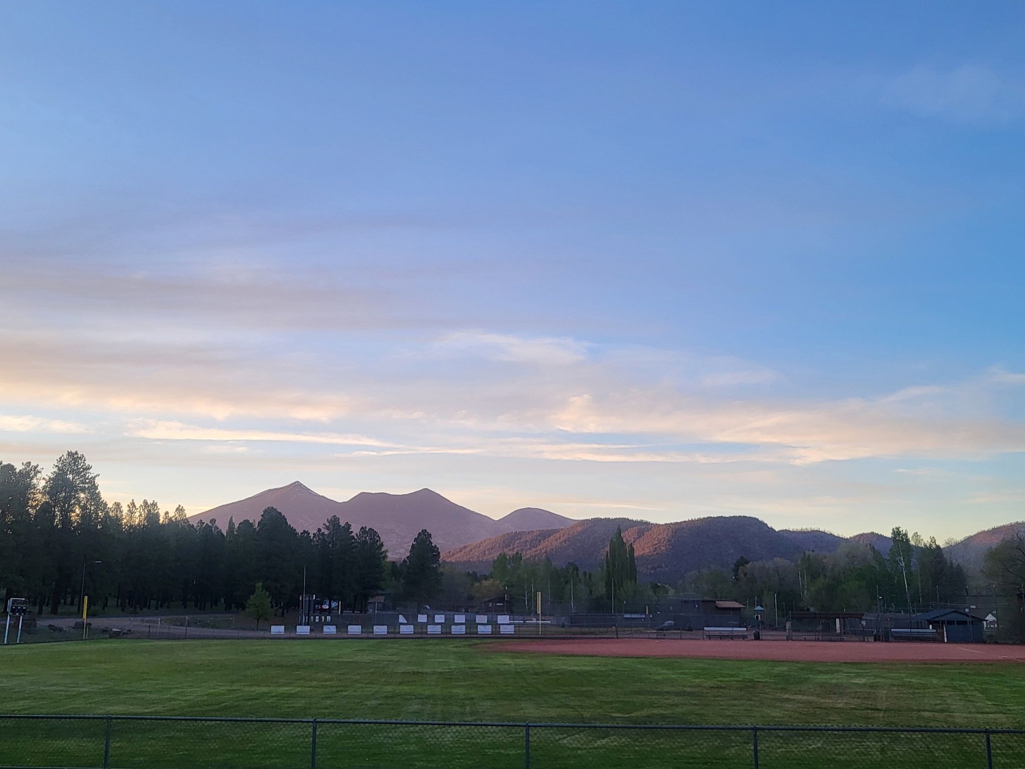 Dusk sky over a baseball field with mountains and pine trees in the background. - Elden Mountain Lookout Tower – Karen Cooper Trailhead loop from Flagstaff