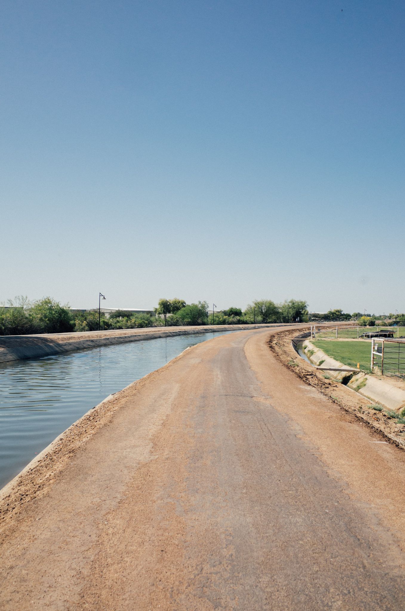 A dirt path runs alongside a calm canal under a clear blue sky. - Sun Circle Trail – Paseo Vista Recreation Area loop from Chandler