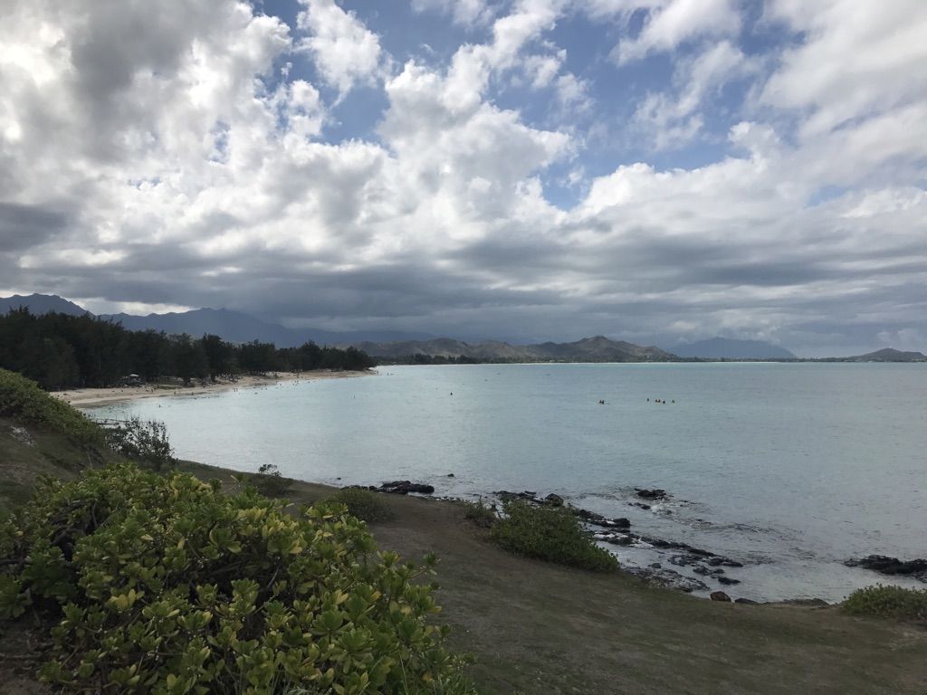 Overcast view of a calm bay with a sandy beach, distant mountains, and boats. - South Lanikai via Kailua Beach loop
