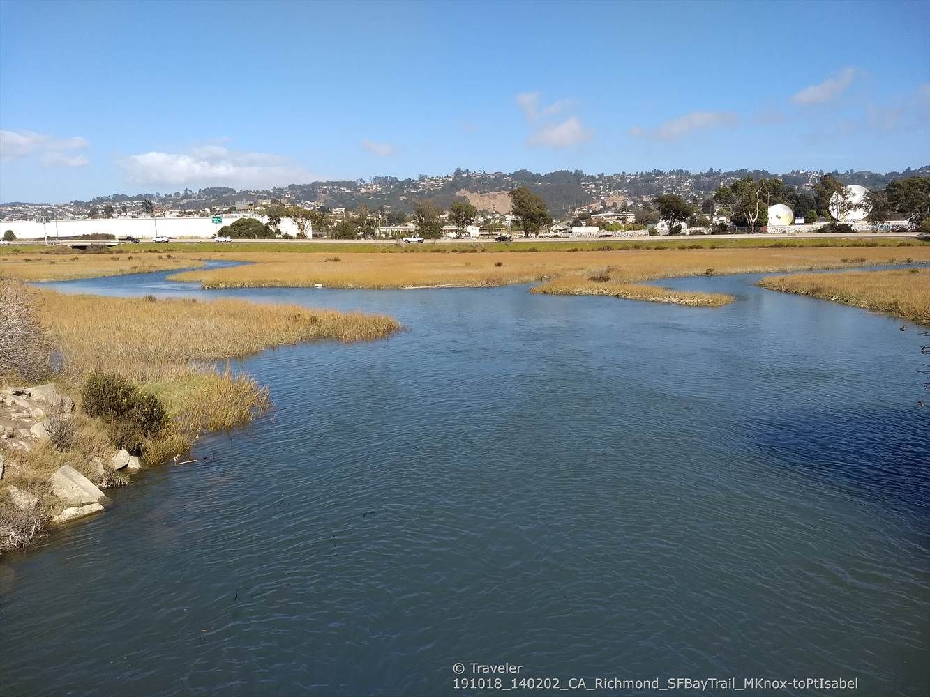River flowing through marshland on a sunny day, with distant town. - Bay Trail at Point Isabel Regional Shoreline