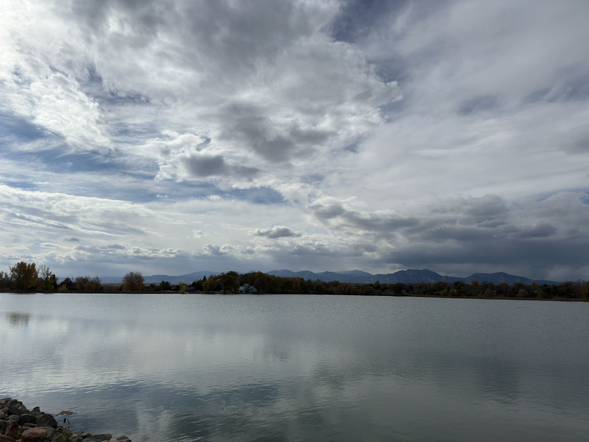 Calm lake reflecting cloudy sky, with distant mountains and trees. - Waneka Lake Trail