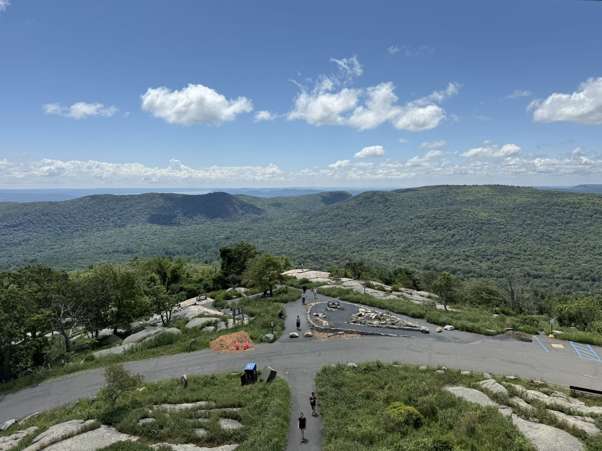 People walk on a rocky summit with panoramic views of distant forested hills. - Perkins Memorial Tower loop from Bear Mountain State Park