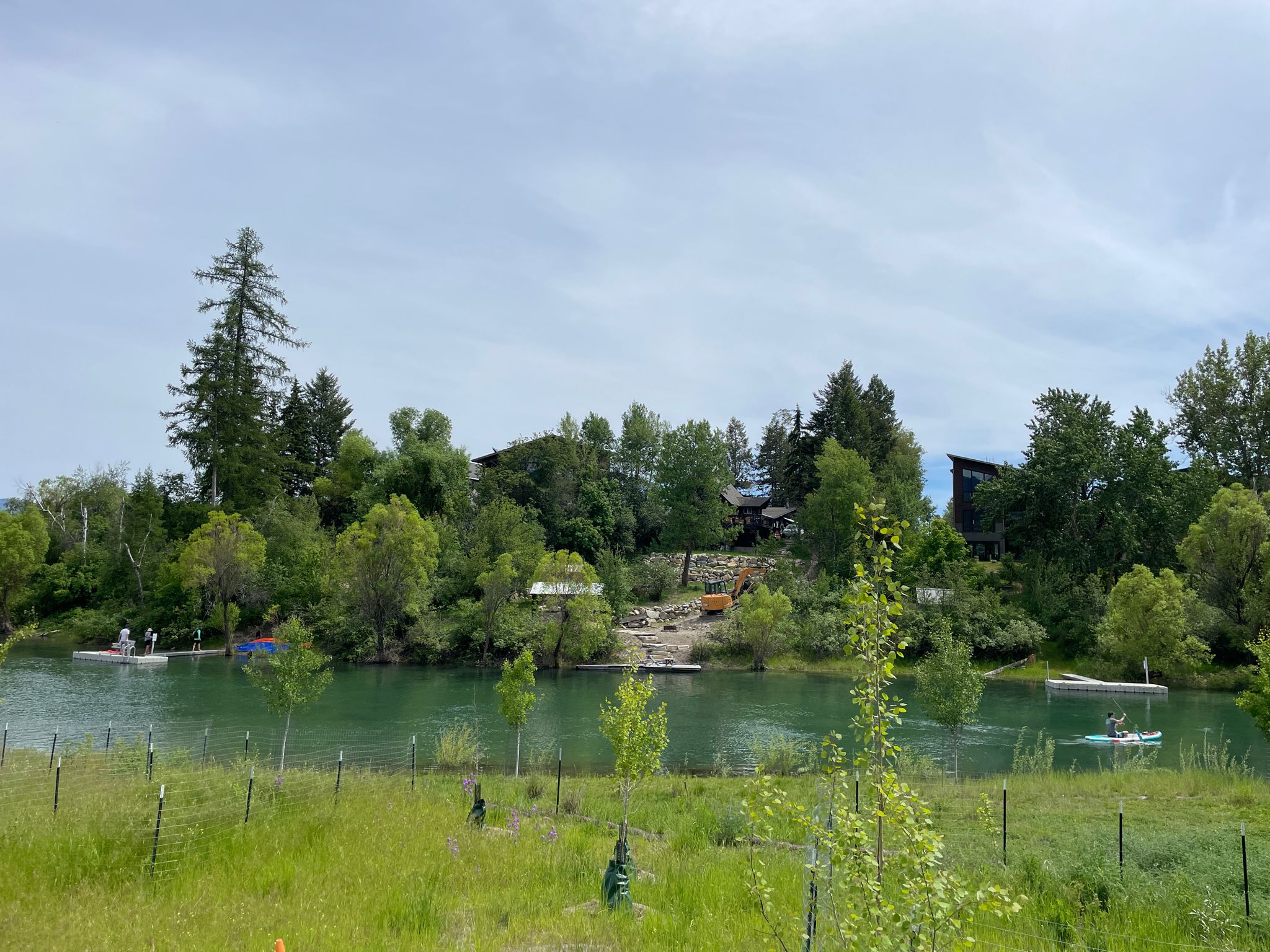 River with paddleboarders, forested banks, and distant buildings under clouds. - Great Divide Mountain Bike Route