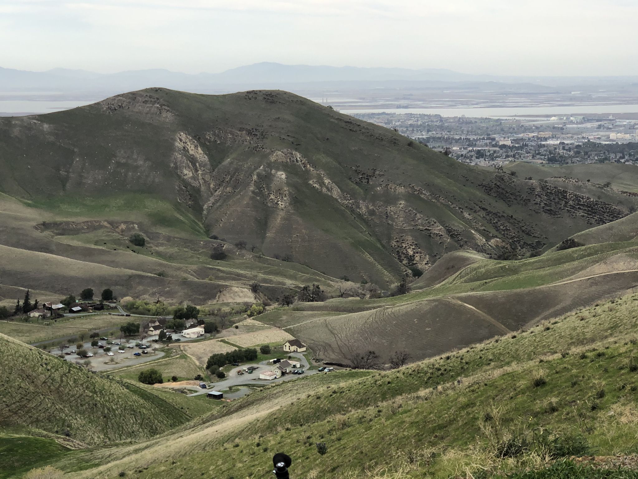 Overcast view of green rolling hills, a valley with buildings, and distant city. - River View and Railroad Bed Trail Loop
