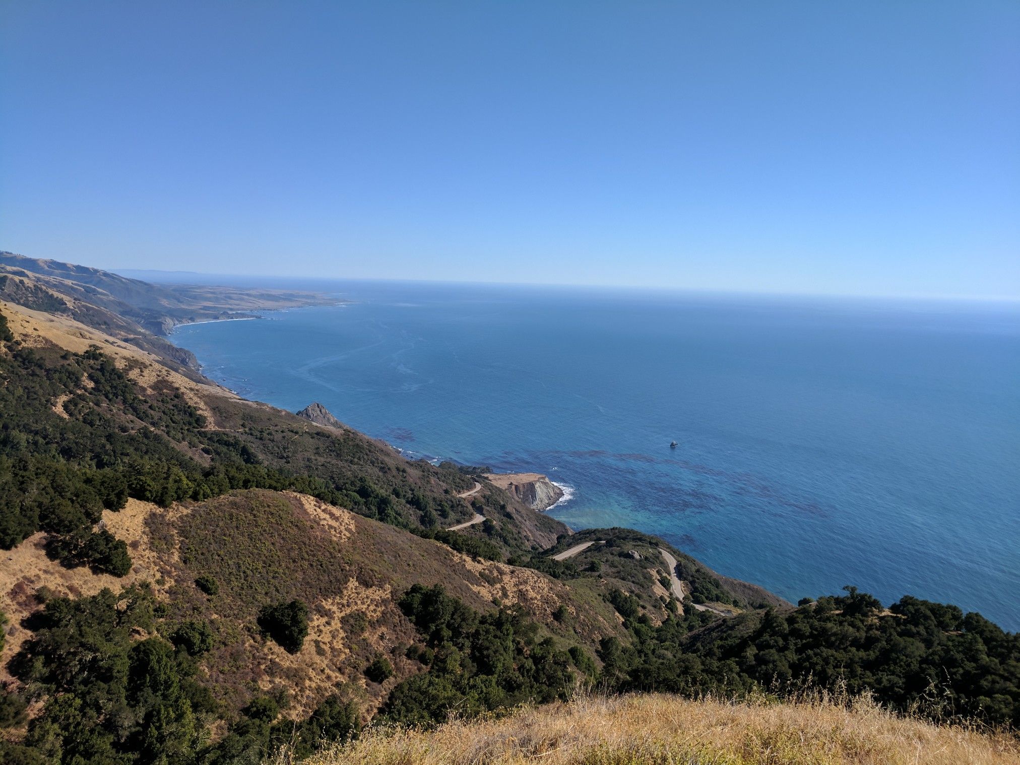 Vast blue ocean meets rugged, green and brown coastal hills under a clear sky. - Buckeye Trail