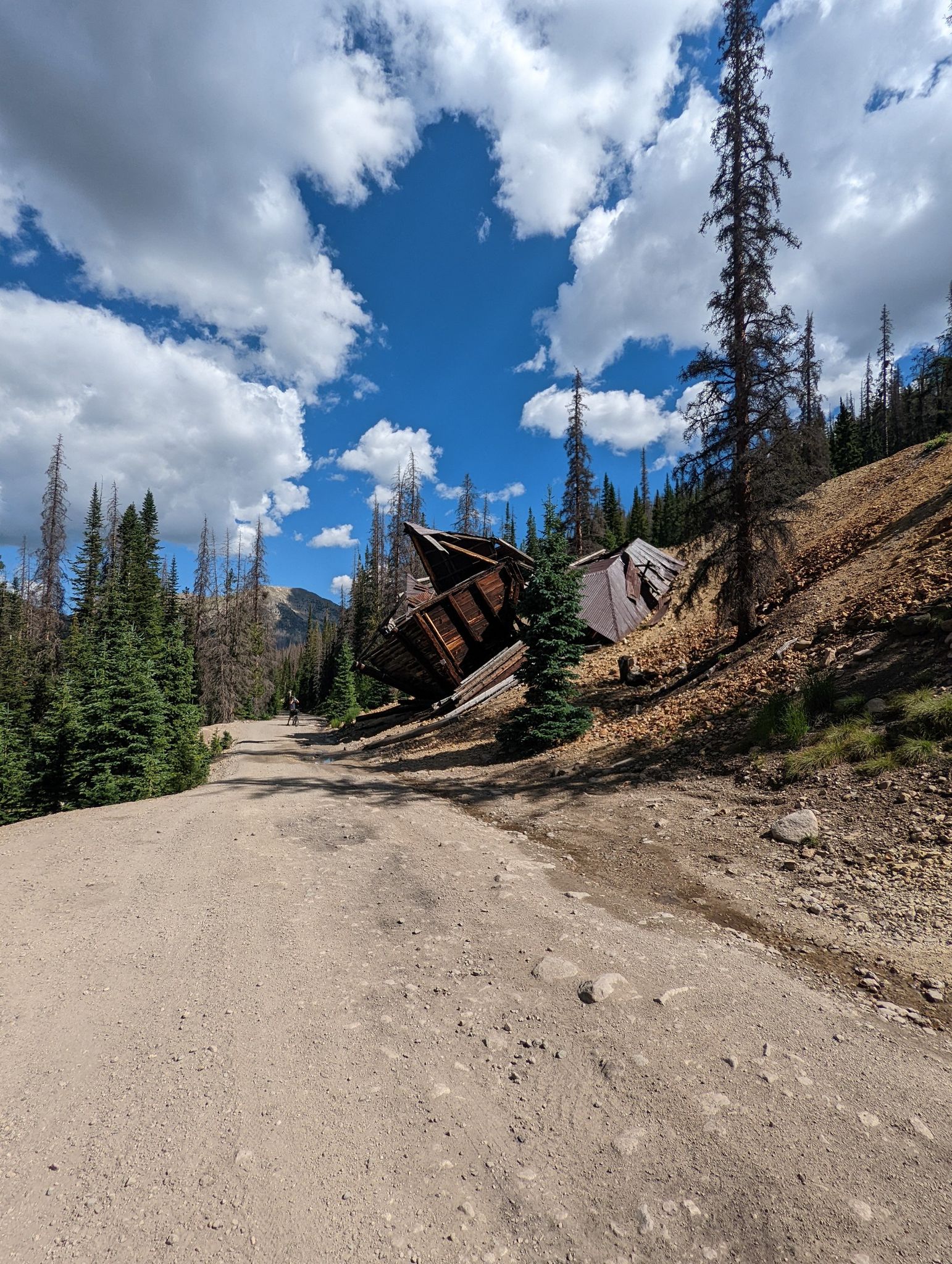 Dilapidated wooden structures on a pine-covered hillside under a partly cloudy sky. - CDT Alpine Tunnel Loop