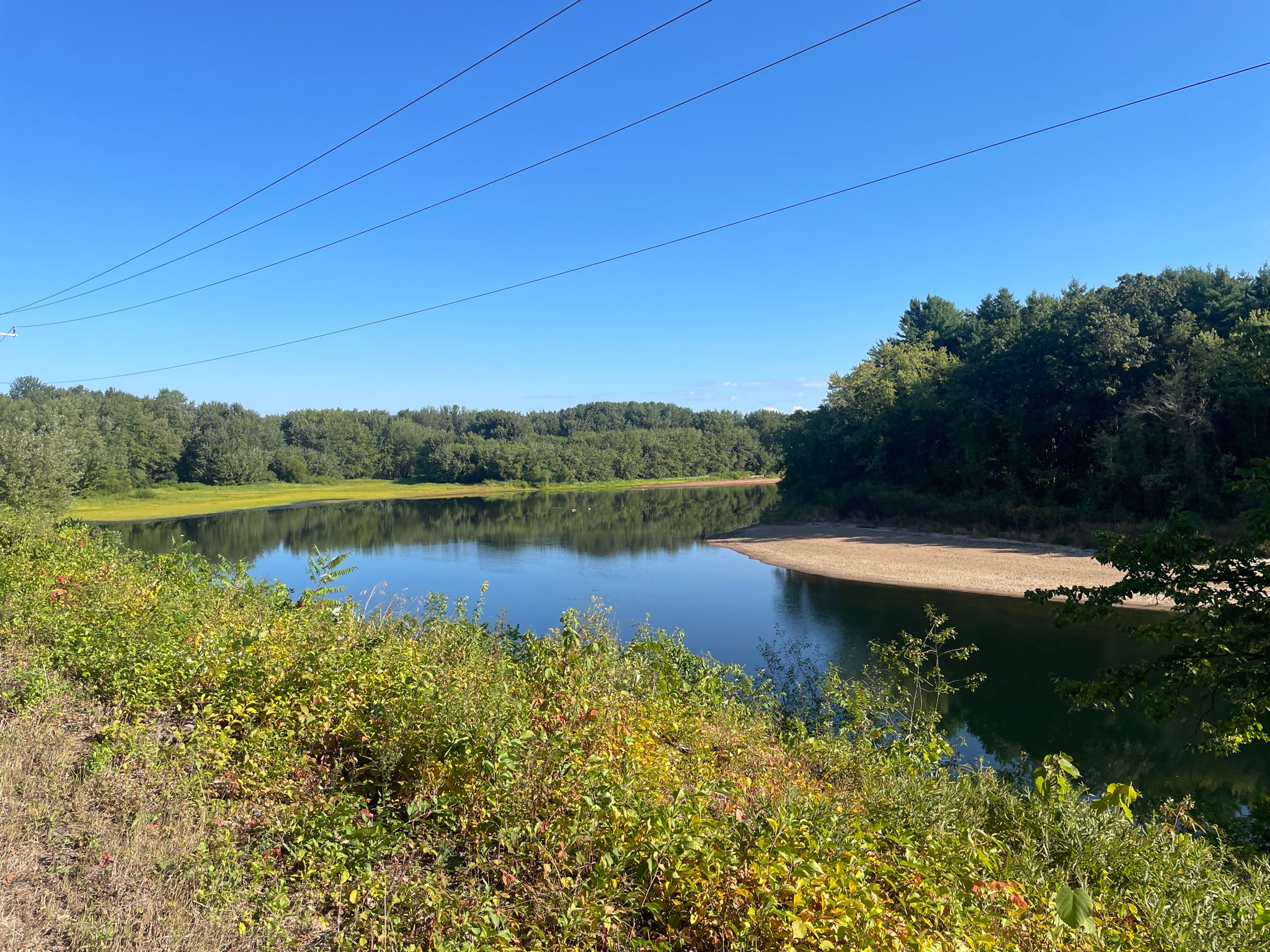 A calm lake surrounded by green trees under a clear blue sky. - Contoocook River road ride loop